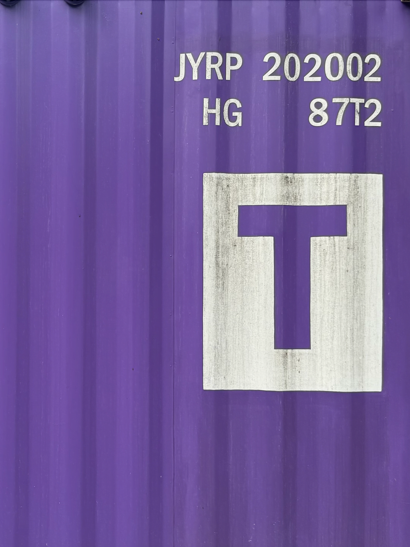 보라색 컨테이너로 만들어진 건물의 벽을 찍은 것이다.'ABVP 202002 HG 87t2'라고 크게 'T'가 적혀있다.