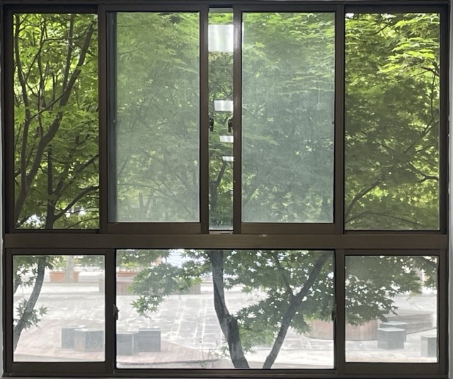 옆으로 밀어서 여는 방식의 중앙고정 창문과 아래에 작은 중앙고정 창문이 함께 있는 사진 갈색의 철제 프레임이며 위의 창문은 열려있다