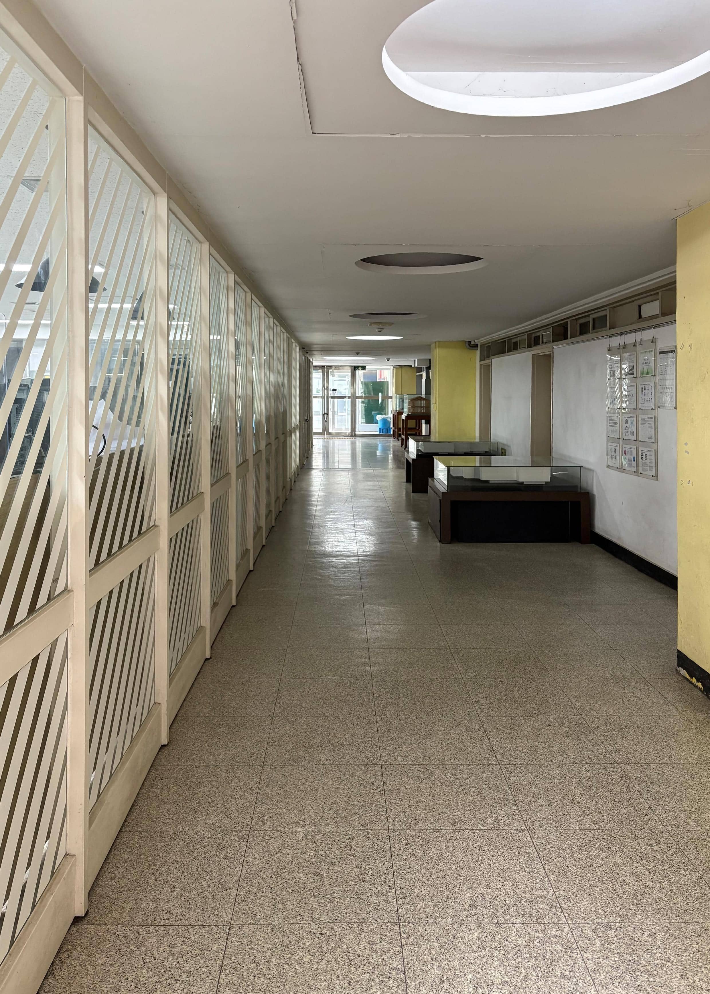 영남대학교 건축관 1층 중복도. 왼쪽엔 불투명한 격자 칸막이와 벽에 달린 문이 있고 오른쪽엔 흰색 벽에 노란 기둥이 있다. 복도 끝에는 유리로 된 출입문이 있다.