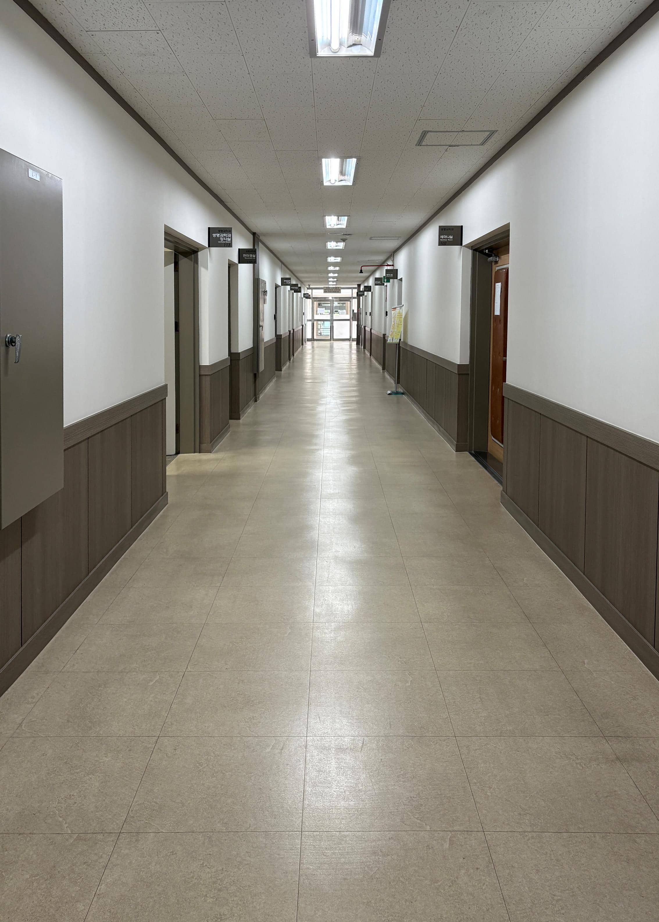 영남대학교 사회과학관 1층 중복도. 왼쪽 벽에는 강사실과 현미경실 등 여러 방들이 있다. 오른쪽 벽에는 세미나실과 다른 방들이 있다. 복도 끝에는 다른 건물로 가는 유리문이 있다. 