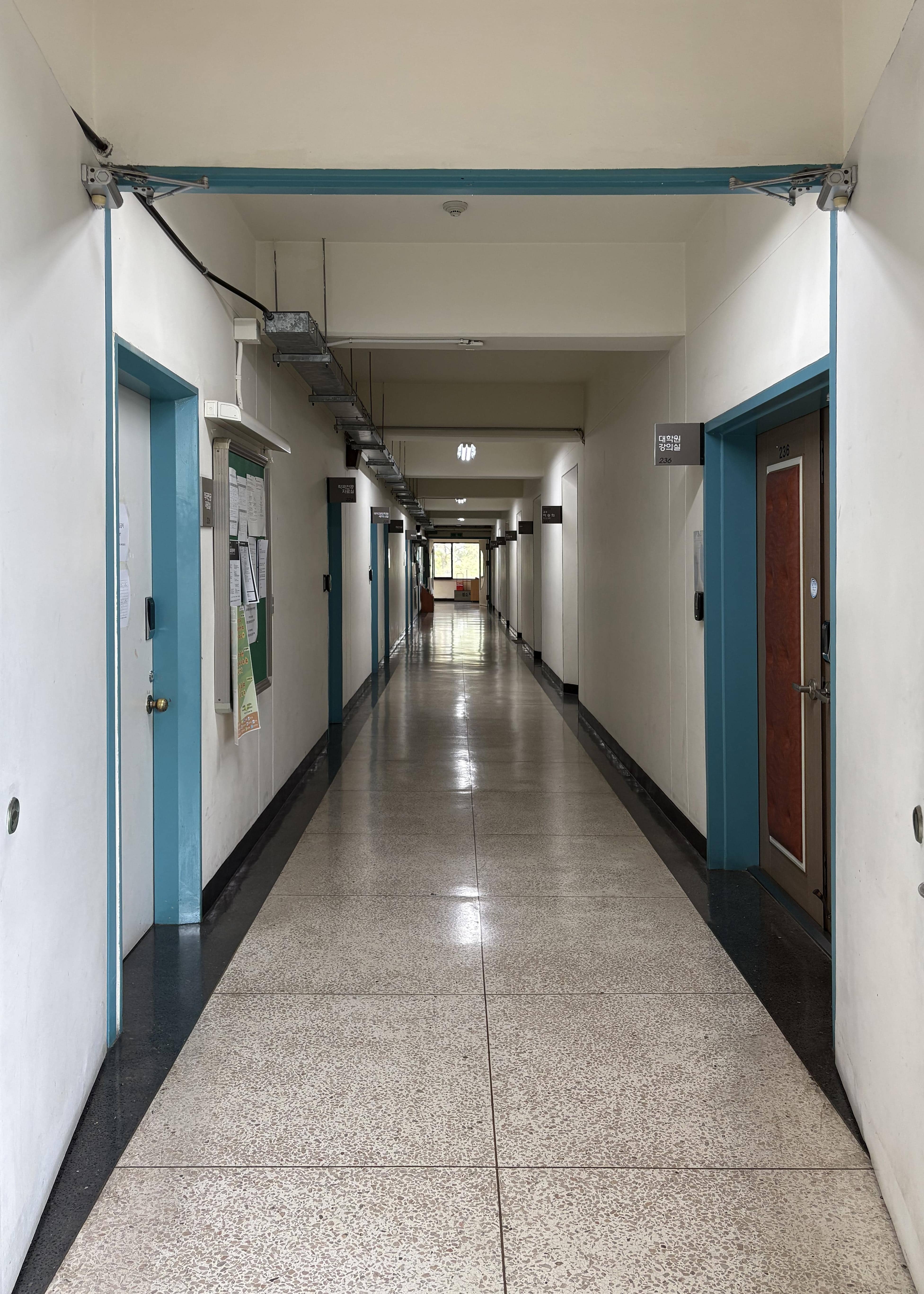 영남대학교 음악관 2층 중복도. 왼쪽 벽에는 자료실이 있고 자료실 옆에는 계시판이 있다. 그리고 여러 강의실들이 여럿 있다. 오른쪽 벽에는 대학원 강의실들이 있다. 복도 끝에는 큰 창문이 있다. 