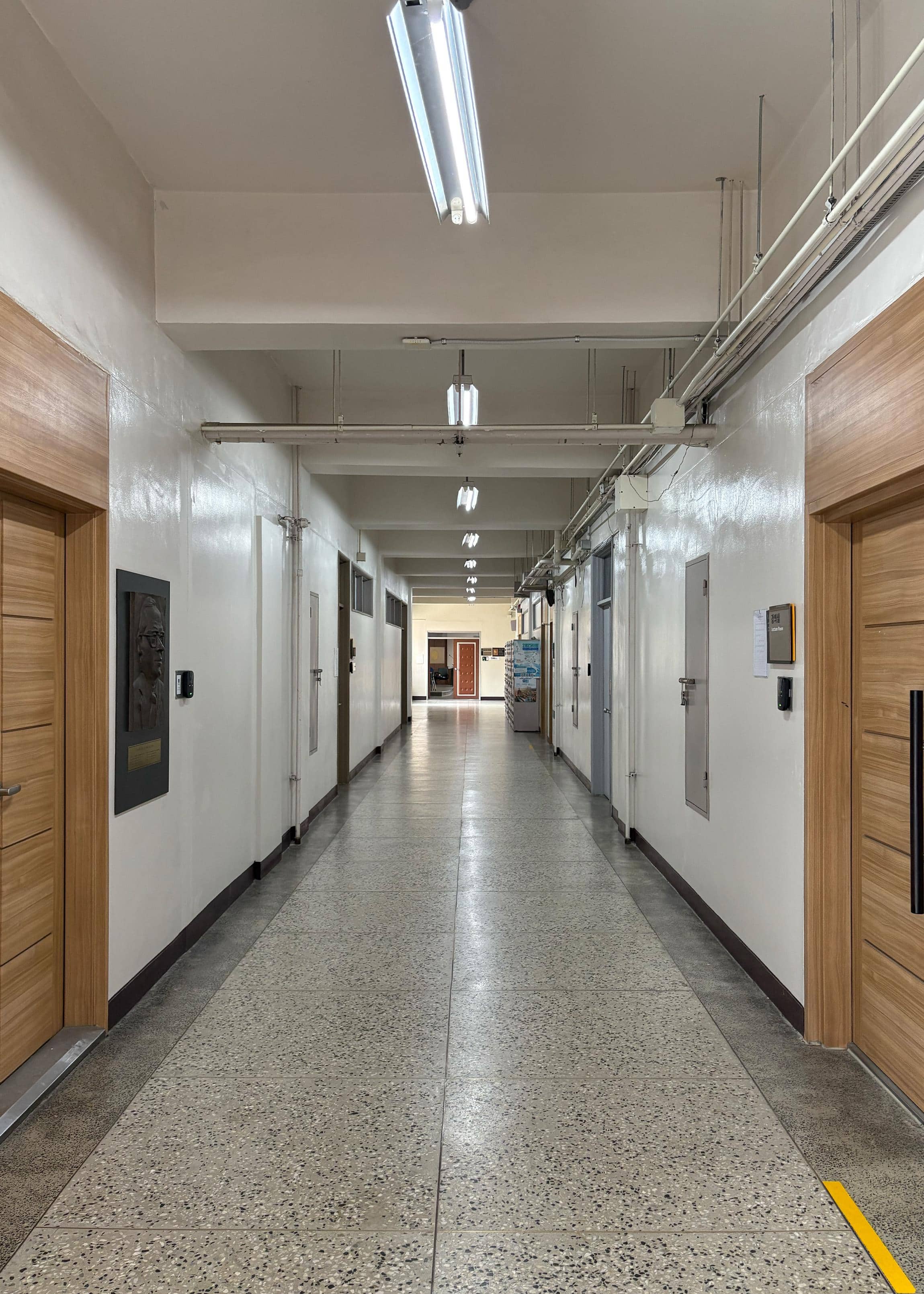 영남대학교 화공관 1층 중복도. 왼쪽 벽에는 갈색문이 3개 있고 흰색으로 벽이 칠해져 있다. 오른쪽 벽에는 갈색 문과 회색 철문이 2개 있다. 복도 끝에는 다른 강의실로 갈 수 있는 문이 있다. 