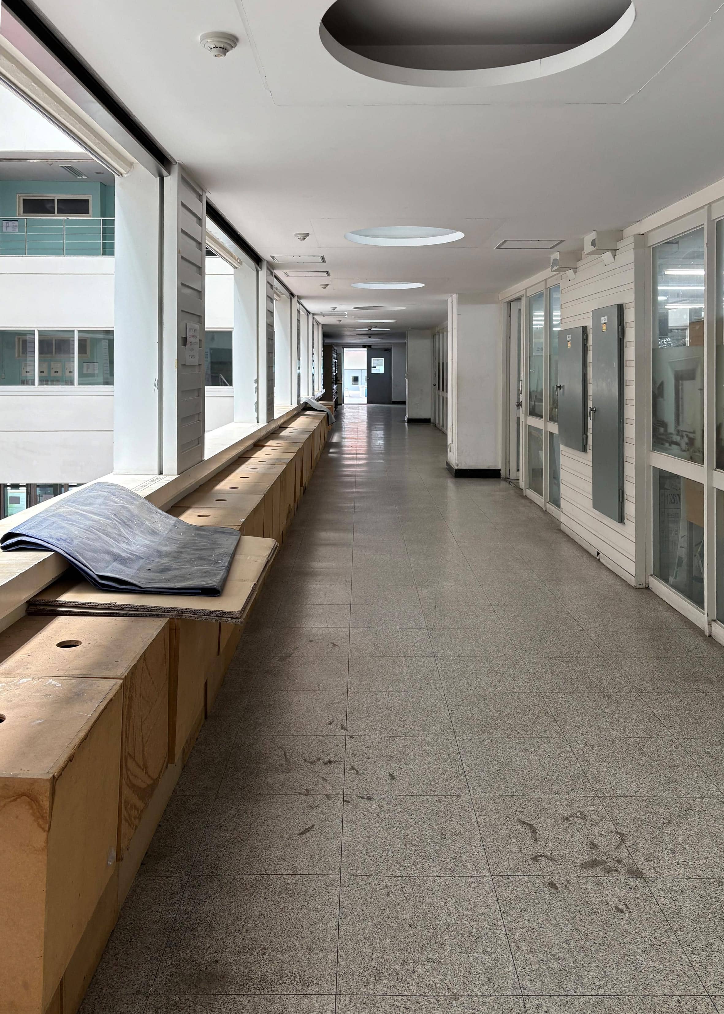 영남대학교 건축관 2층 편복도. 왼쪽 벽에는 나무로 된 사물함과 흰색 난간, 기둥이 있다. 오른쪽 벽에는 컴퓨터실로 갈 수 있는 유리문이 있다. 복도 끝에는 다른 건물과 이어져 있는 구름다리가 있다.