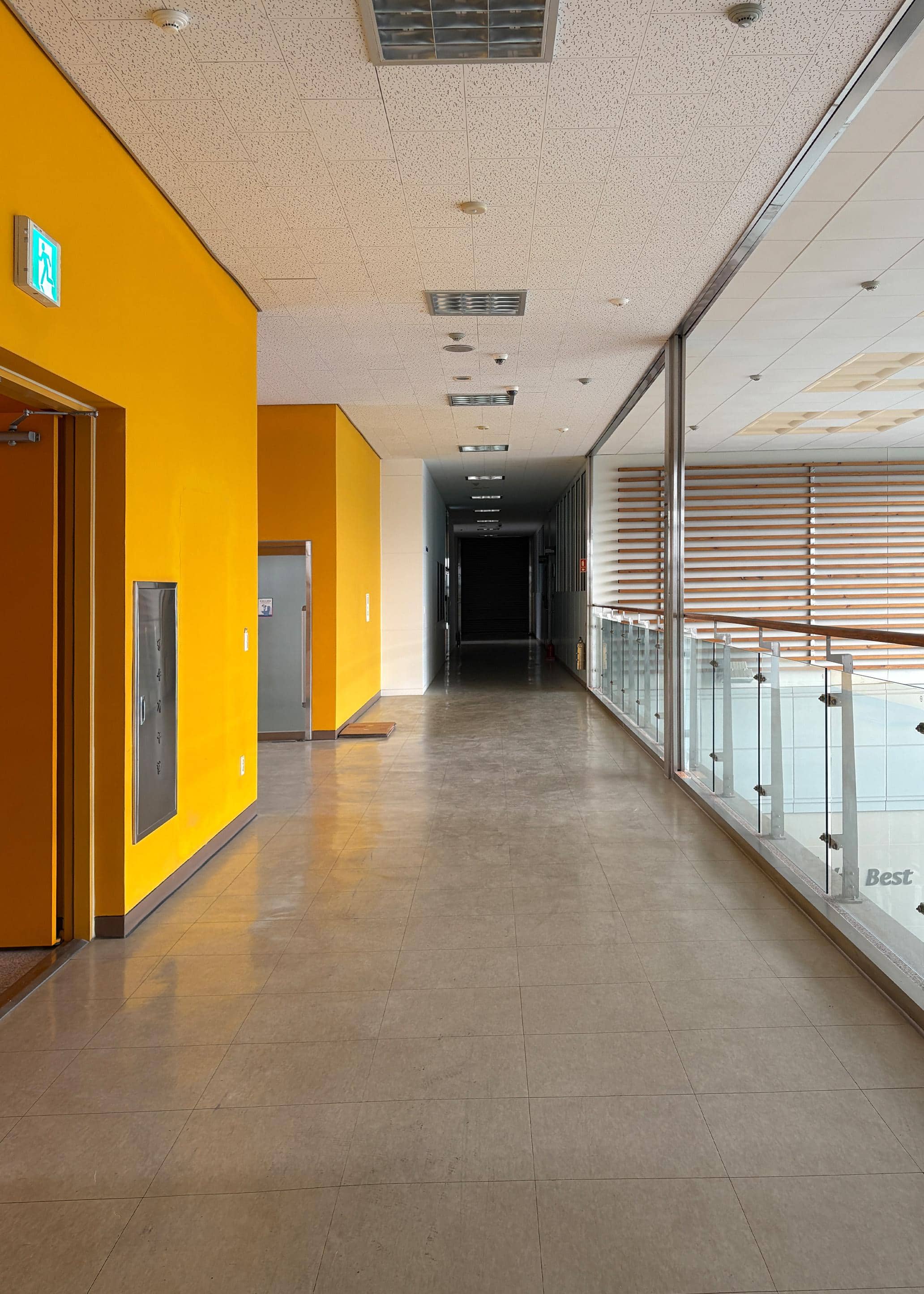 영남대학교 산학협력단 2층 편복도. 왼쪽 노란 벽에는 비상계단과 화장실이 있다. 오른쪽 벽에는 유리로 된 난간이 있다. 복도 끝에는 어둠으로 이루어져있다.
