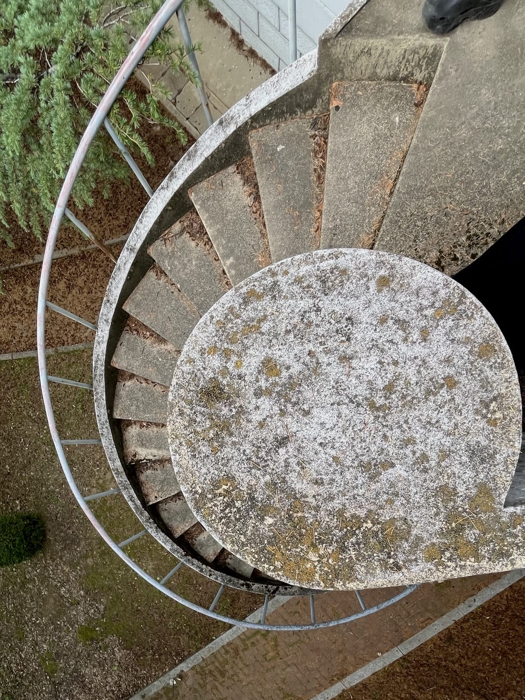 흰색 기둥을 가준으로 돌아가는 탁한 갈색 타일의 나선형 계단을 위에서 내려다본 사진.가장자리를 따라 은색 금속 난간이 보인다.