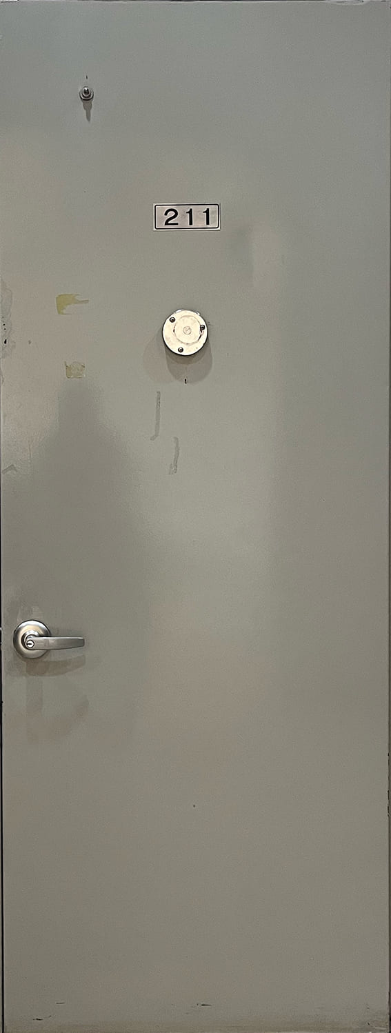 영남대 전시실로 들어가는 문이다.닫겨있고 회색 철문이다.문에 211이라는 숫자가 붙어있다. 숫자 아랫쪽에는 둥글고 납작한 금속이 붙어있다.가로로 긴 철 손잡이가 문의 왼쪽 중앙에 달려있다.