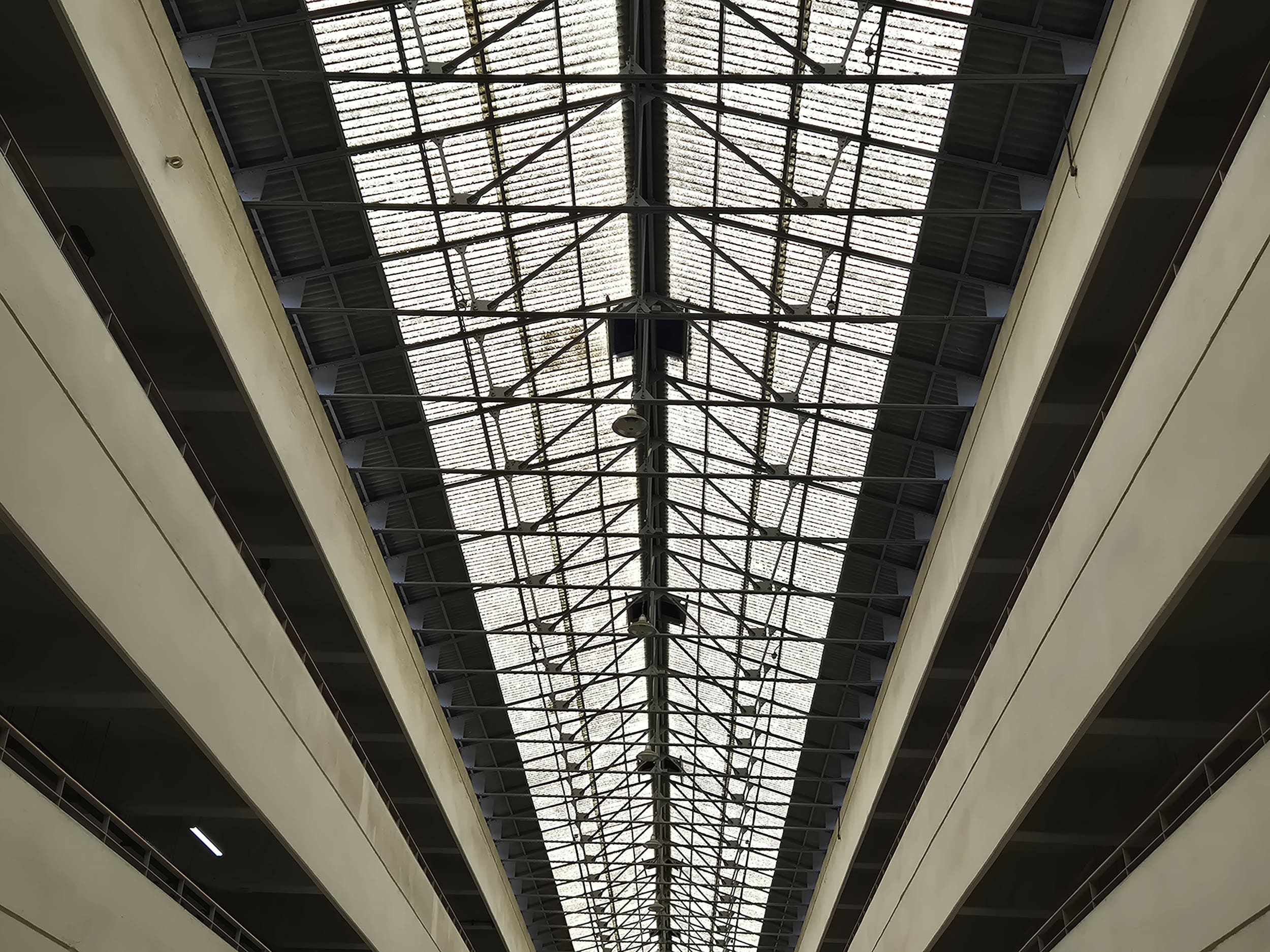 철제 트러스가 반복적으로 구성되어 있는 구조의 천장 사진이다. 중앙 부분이 가장 높고 좌우로 경사가 있는 천장 모습을 하고 있으며, 철제는 회색, 양쪽 벽면은 황갈색을 띠고 있다.