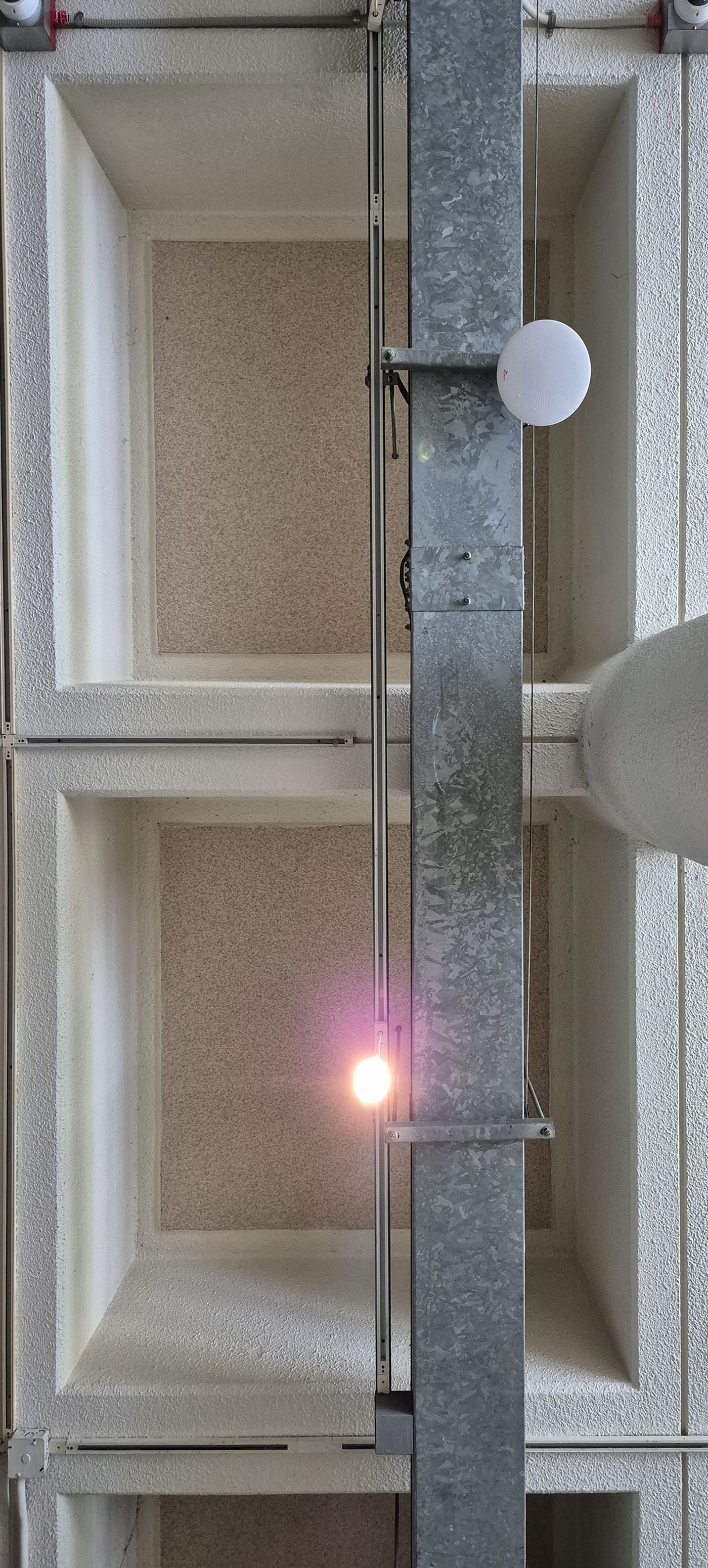 사각형 격자 형태로 나열된 구조의 천장 사진이다. 천장의 격자 부분은 아이보리색이고, 격자 안쪽의 천장 색은 옅은 황갈색 빛을 띤다. 오른쪽에 세로로 긴 기둥이 있다. 중앙에서 아랫쪽 부분에는 밝게 빛나는 작은 조명이 설치되어 있다. 천장을 정면에서 찍은 세로로 긴 사진이다.