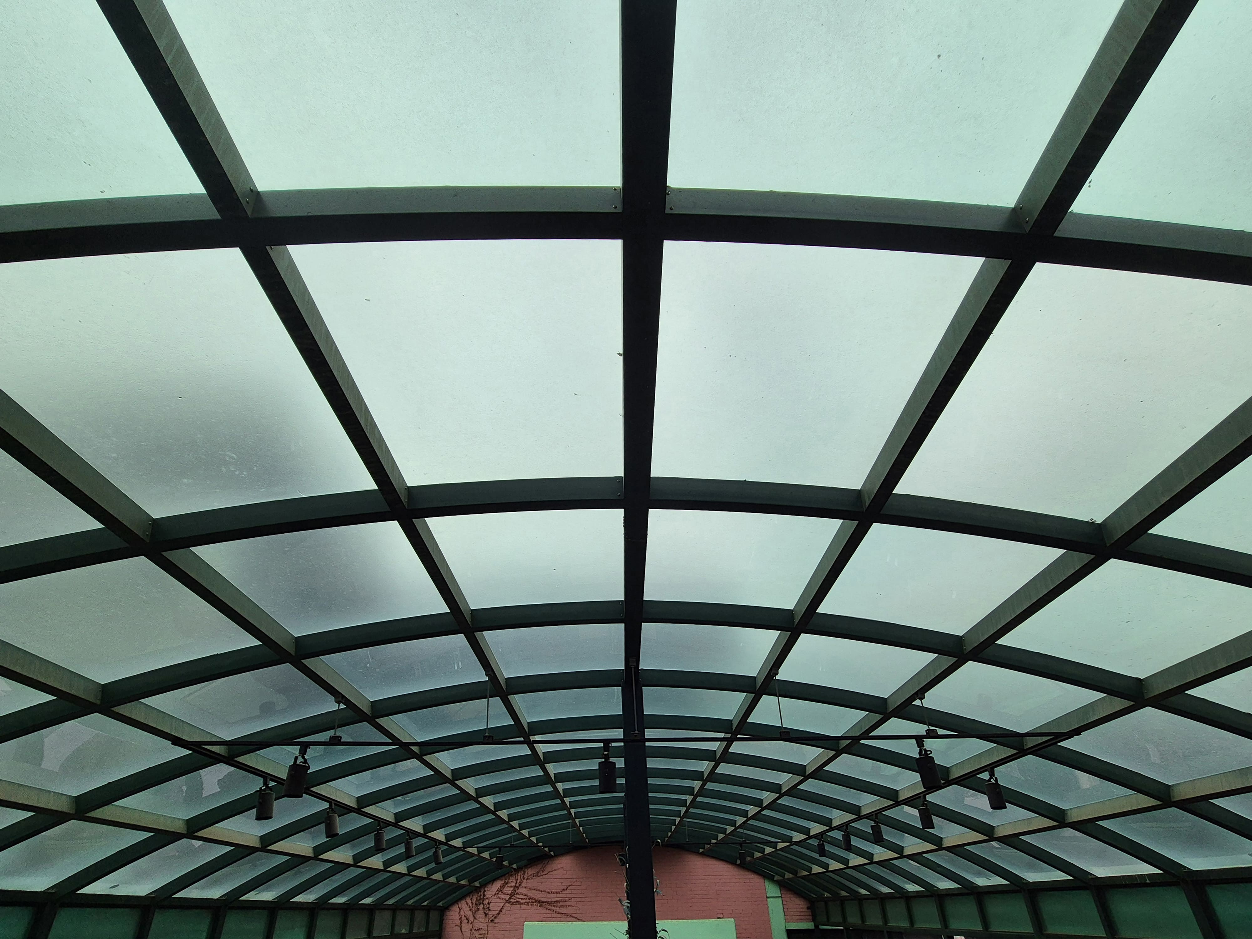 곡선 형태의 초록빛 철제 프레임과 연한 초록빛 반투명 지붕의 구조를 가진 천장 사진이다. 원근감이 느껴지는 사진이다.