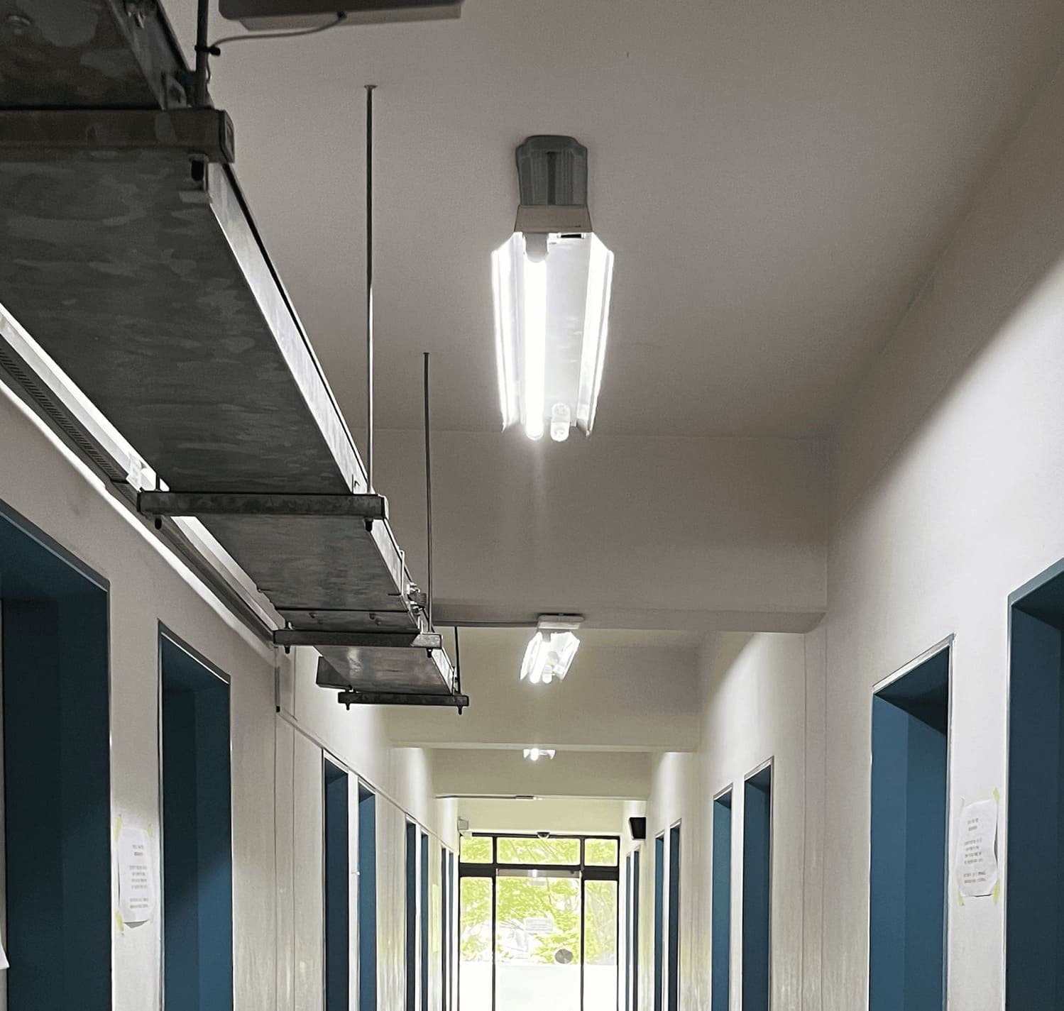 소실점이 중앙에 있는 복도의 중간부터 천장까지의 사진. 천장에는 천장에는 규칙적으로 보가 튀어나와있다. 보가 없는 들어간 부분엔 하나씩 노출형 형광등 2구가 매달려있다.양쪽 벽은 대칭으로 이루어져 각각 7개의 문틀이 보임. 문틀은 모두 짙은 하늘색이다. 복도 끝에 있는 밖으로 나가는 유리문이있다. 2번 복도의 위.