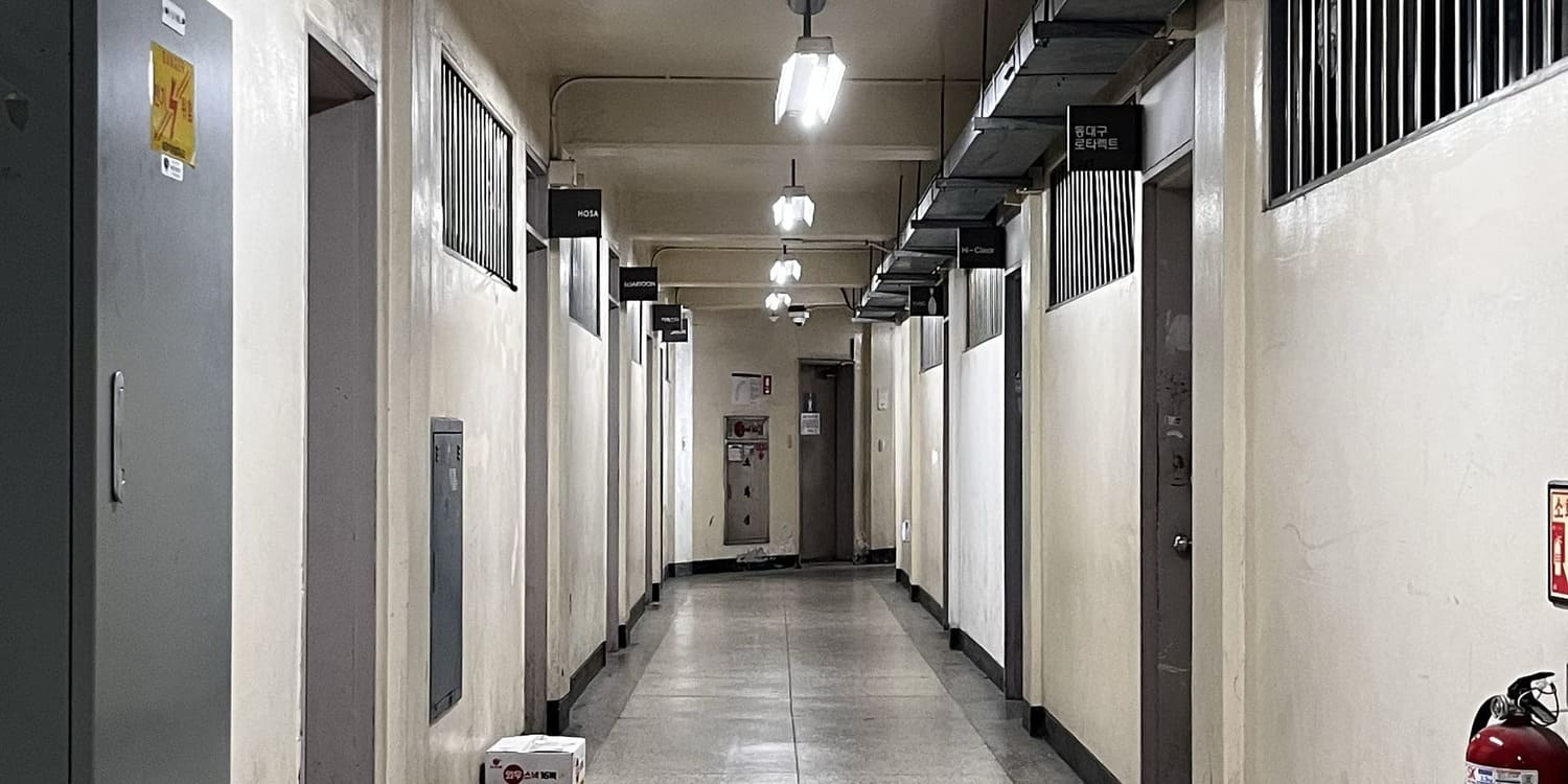 중간에 소실점이 있는 사진을 세로로 3분할 한 사진의 중간. 왼쪽 벽에는 철제 전기 관리함이 매달려있고 연보라빛의 철제 문틀과 문, 철창이 있는 창문이 반복적으로 있다.오른쪽 벽 아래에는 소화기의 윗부분이 살짝 잘려있으며 위에는 철제 창살이 있는 창문이 3개, 사이사이 철제 문과 문틀이 위치해있다. 오른쪽 천장에는 덕트가 있다.1번 사진의 중간.