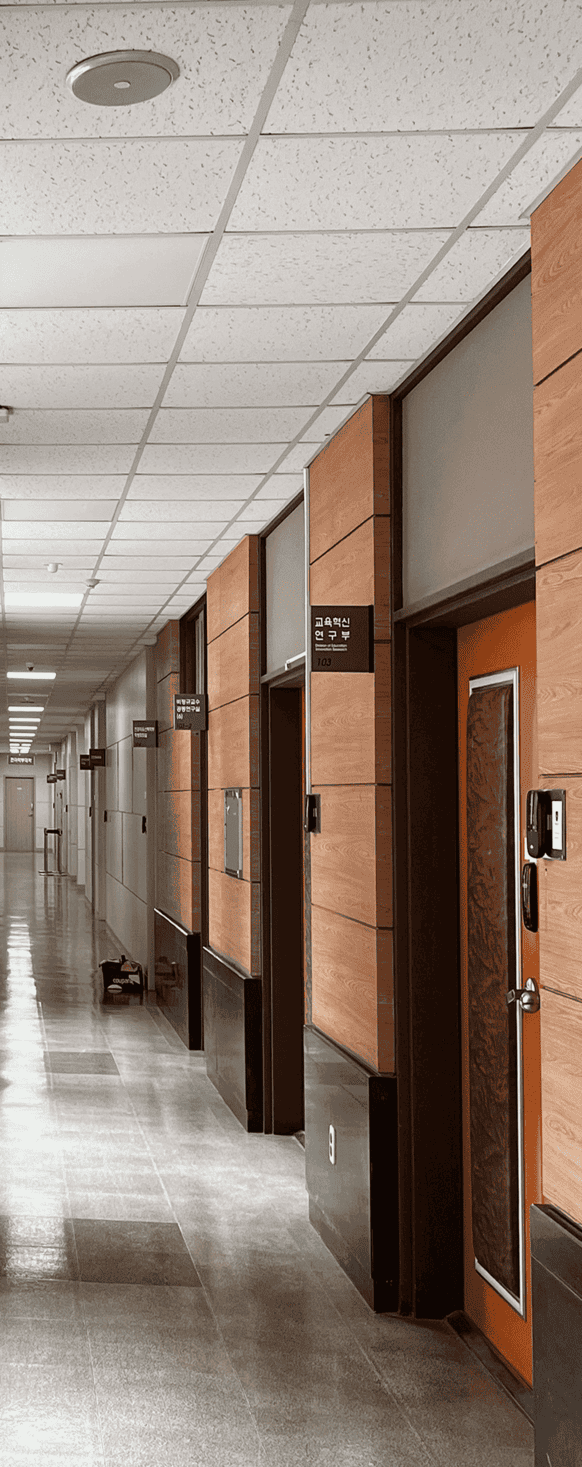  중앙에 소실점이 위치한 채 찍힌 사진의 중앙부터 오른편까지의 절반. 사진오른쪽에 교육혁신 연구원, 비정규교수 공통연구실 등 여러 방의 문이 나열되어있다. 문틀은 어두운 갈색이며 주황색 문, 중간에는 갈색의 세로로 긴 사각형 쿠션이 설치되어 있다 벽은 사진을 기준으로 가까운 곳에서 중간까지 붉은 빛이 도는 밝은 갈색 타일이며 아래는 검정색 유광 마감이 되어있다. 절반부터 가장 먼 곳까지는 흰색 타일이며 천장도 흰색의 정사각형 타일로 이루어져있다.