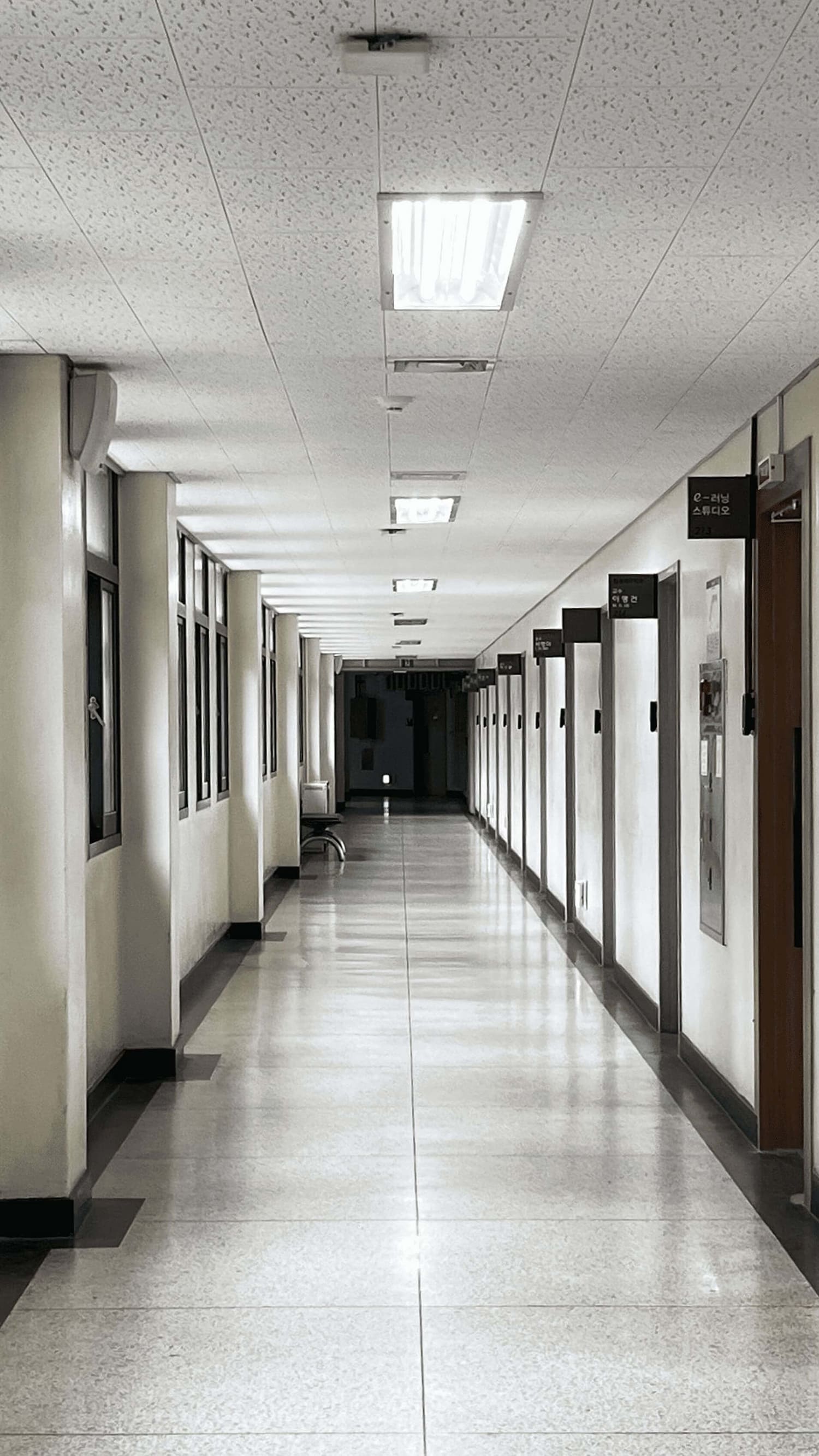 오른쪽에는 e러닝 스튜디오를 포함한 여러개의 방이 있는 복도 사진. 오른쪽에는 청록색의 직사각형 창문과 스피커가 설치되어있다. 바닥은 테라조 타일, 천장은 흡음텍스 천장으로 직사각형의 매입형 형광등이 설치되어있다.