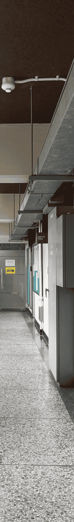 중간에 소실점이 모이는 복도를 세로로 4분할 했을 때의 왼쪽에서 세번째 사진. 콘크리트 천장과 벽. 천장에는 보가 내려와있으며 들어간 부분에는 검붉은색 칠이 되어있고 덕트가 매달려있다. 복도 끝에는 유리문과  있다. 문틀은 철제로 되어있고 바닥은 테라조 타일. 오른쪽 벽에는 철제함이 벽 절반 사이즈, 벽을 채우는 사이즈 두 개가 있고 인문학과 자료실과 게시판 두 개가 있다. 