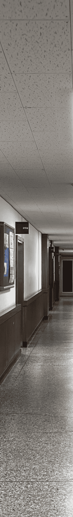 중간에 소실점이 모이는 복도를 세로로 4분할 했을 때의 왼쪽에서 두번째 사진. 콘크리트 몰딩에 아랫부분은 나무몰딩된 부분이 튀어나와있다. 왼쪽 벽에는 게시판과 강의실 안내판, 나무몰딩 문틀이 있다. 천장은 흡음택스천장.