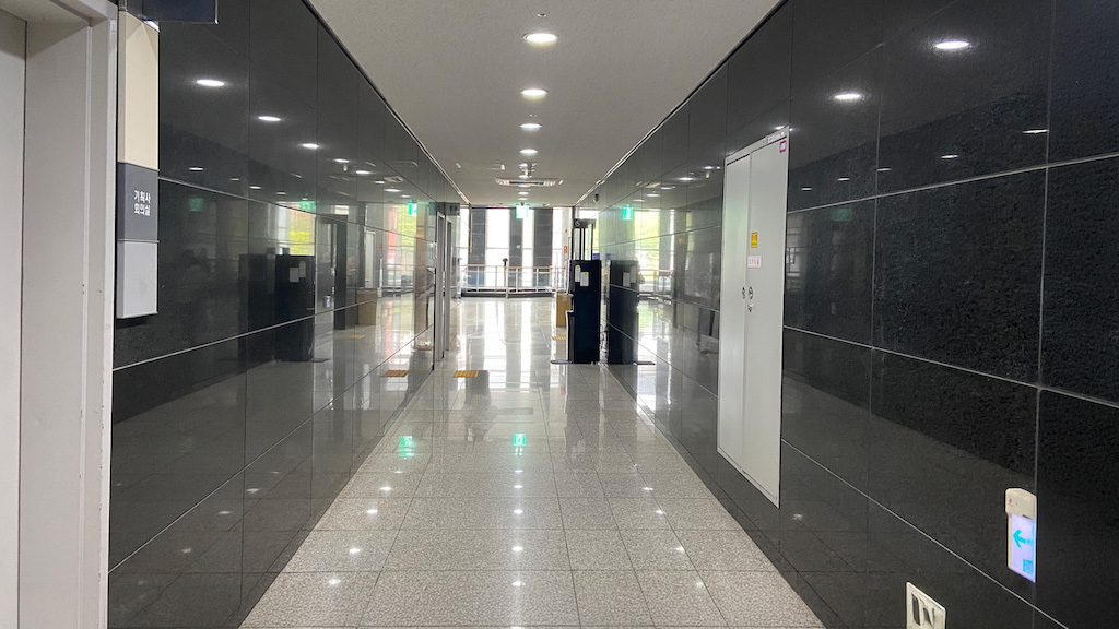 영남대학교 천마아트센터 복도 이미지. 앞으로 길게 복도가 이어져있다. 양 옆에 검정색 벽은 바닥을 반사하고 있다.