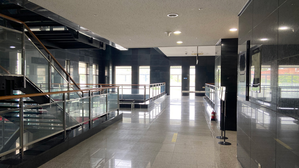 영남대학교 천마아트센터 복도 이미지. 앞으로 복도가 이어져있다. 왼쪽에는 윗층으로 올라갈 수 있는 계단이 있다. 오른쪽에는 팻말이 세워져있다..