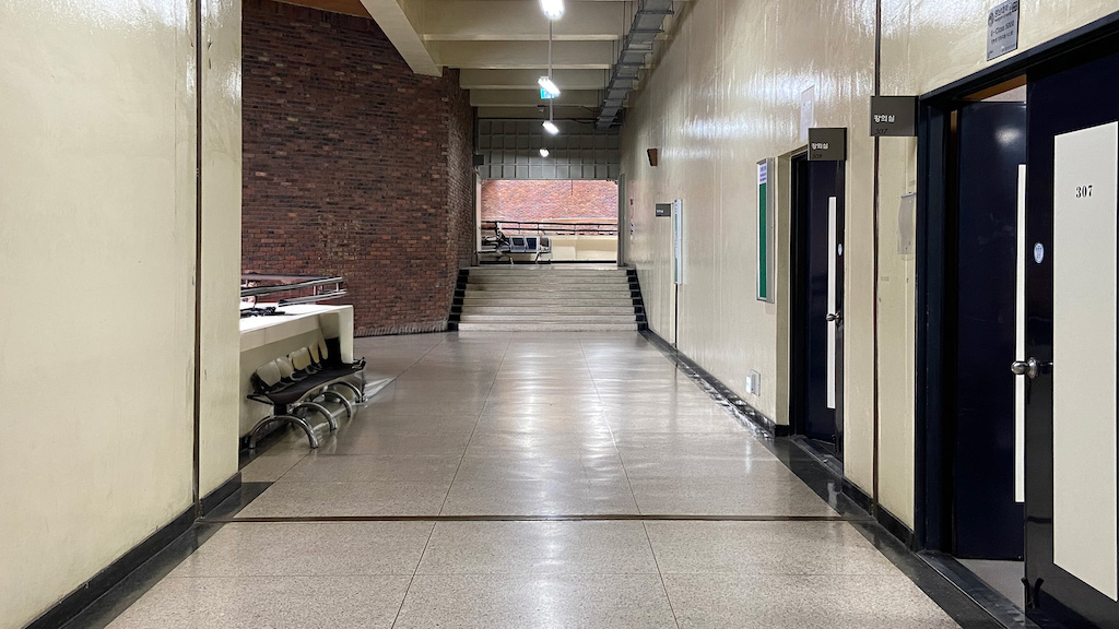 영남대학교 상경관 이미지. 앞에는 계단이 있다. 그 위로 복도가 이어져있다. 옆에는 남색에 가운데에는 불투명한 유리로 만들어진 강의실 문이 있다.