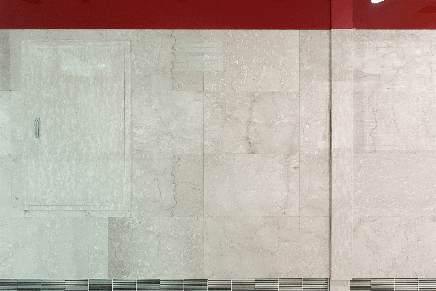대리석 질감의 베이지색 벽이 사진의 전체 화면에 보인다. 벽의 윗부분은 붉은색의 대리석벽이 약간 보이며 사진의 왼쪽엔 작은 대리석 문이 보인다.
