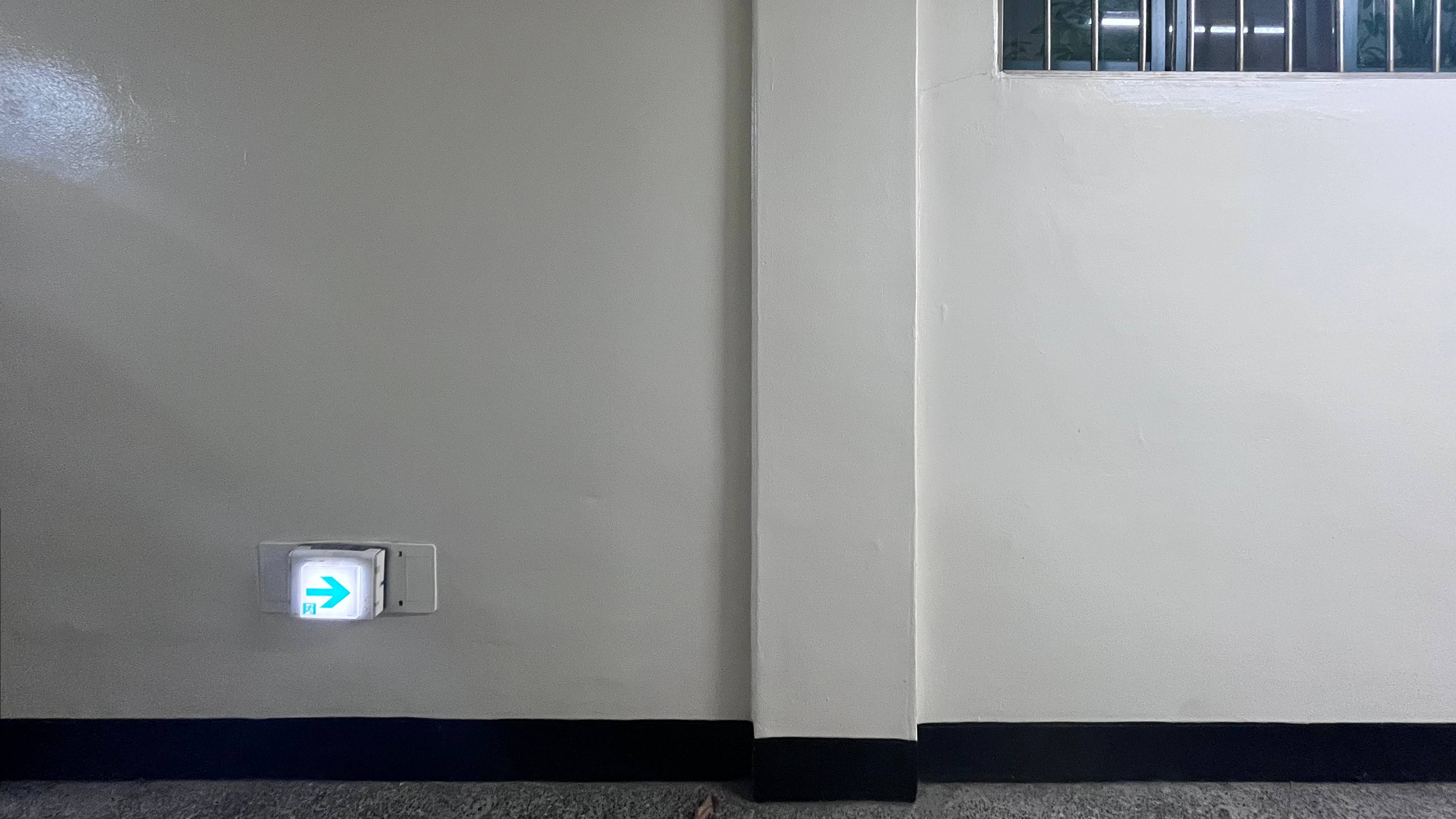 광택이 있는 연회색 벽에 낮게 설치된 비상구 표시등과 검은색 줄무늬가 있다.