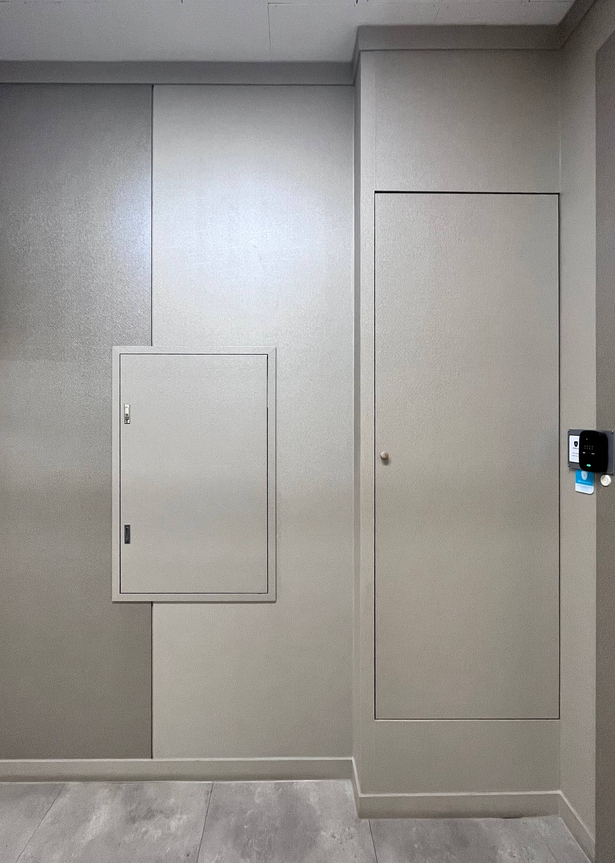 연한 회색빛 톤의 벽으로 오른쪽에는 전자식 카드리더기와 도어락이 붙어있다. 벽면은 서로 다른 크기의 직사각형 패널로 나뉘어져있다.