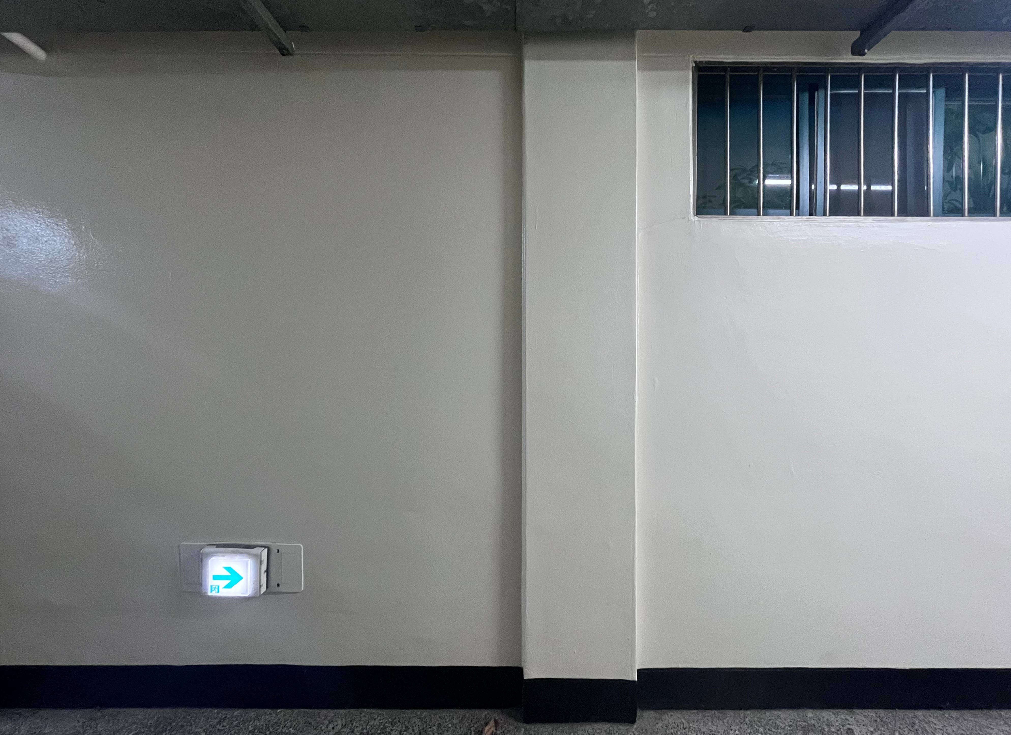 전체적으로 차가운 흰색의 벽면. 매끈하고 광택이 나는 페인트로 마감되어 있으며, 바닥과 맞닿는 부분은 검은색 띠처럼 마감되어 있다. 벽면 왼쪽 아래에는 작고 정사각형 모양의 비상구 표시등이 부착되어 있다. 화면 중앙에는 벽에서 조금 돌출된 기둥이 자리잡고 있다. 오른쪽 상단에는 작은 창문이 설치되어 있다. 