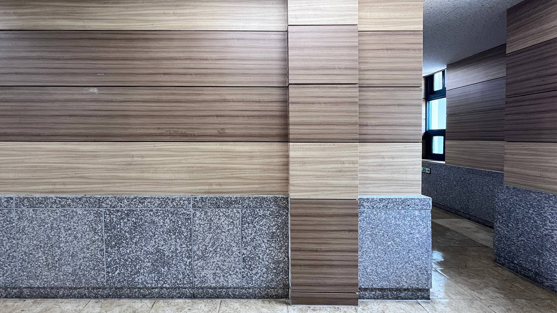 따뜻하고 안정된 느낌의 벽. 연한 갈색과 진한 갈색이 번갈아 반복되며 나무결의 자연스럽다. 벽의 아랫부분은 차가운 회색빛 돌로 마감되어 있다. 정사각형 타일이 수평과 수직으로 정렬되어있다. 중앙에는 나무 판넬이 돌출된 벽 기둥처럼 수직으로 세워져 있다.