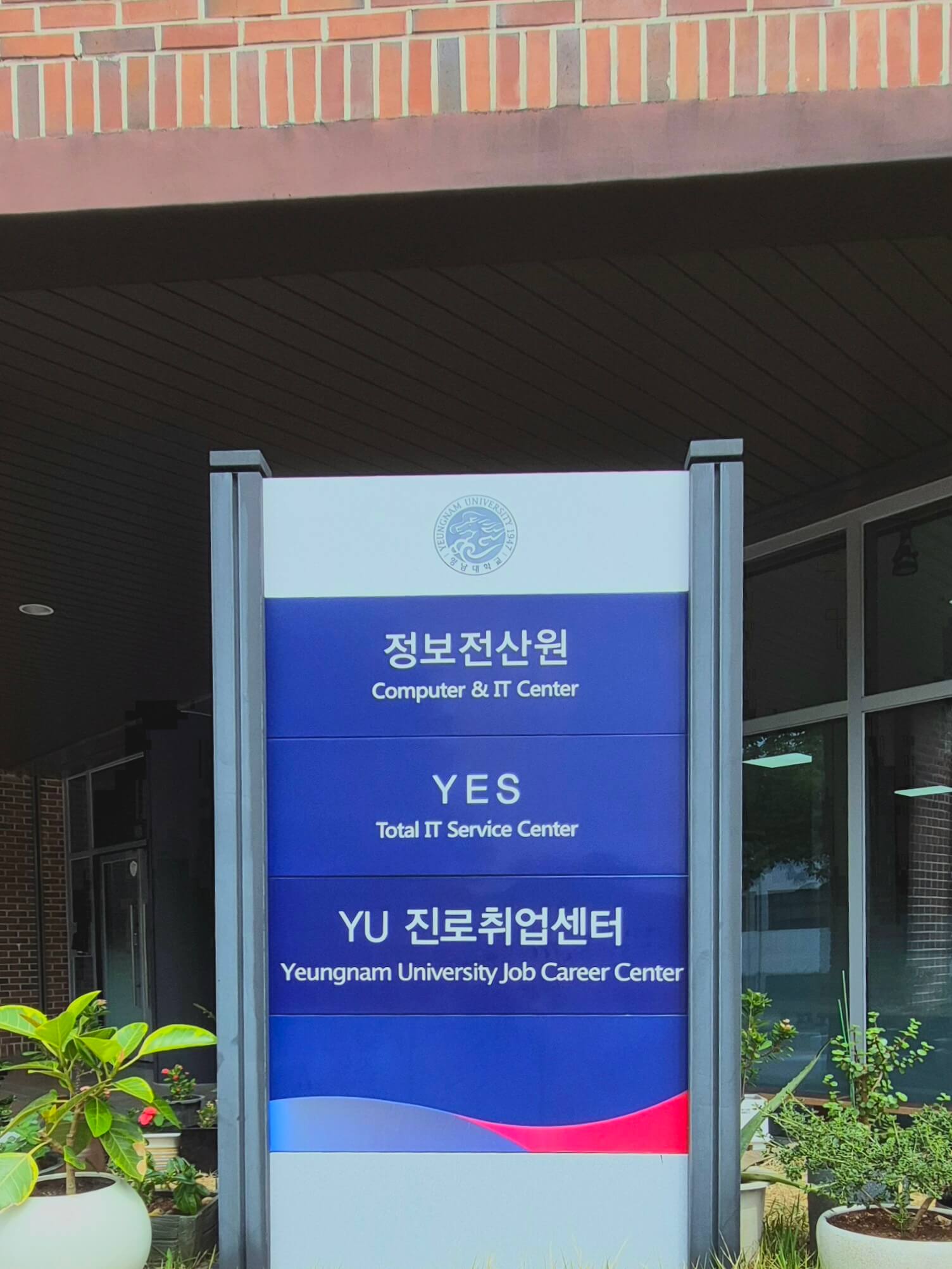 영남대학교의 건물 안내판. 파란색 배경 위로 흰 글씨로 '정보전산원','YES','YU 진로취업센터'라고 적혀있고 각각 글씨 밑에 작게 영어 번역이 적혀있다.
