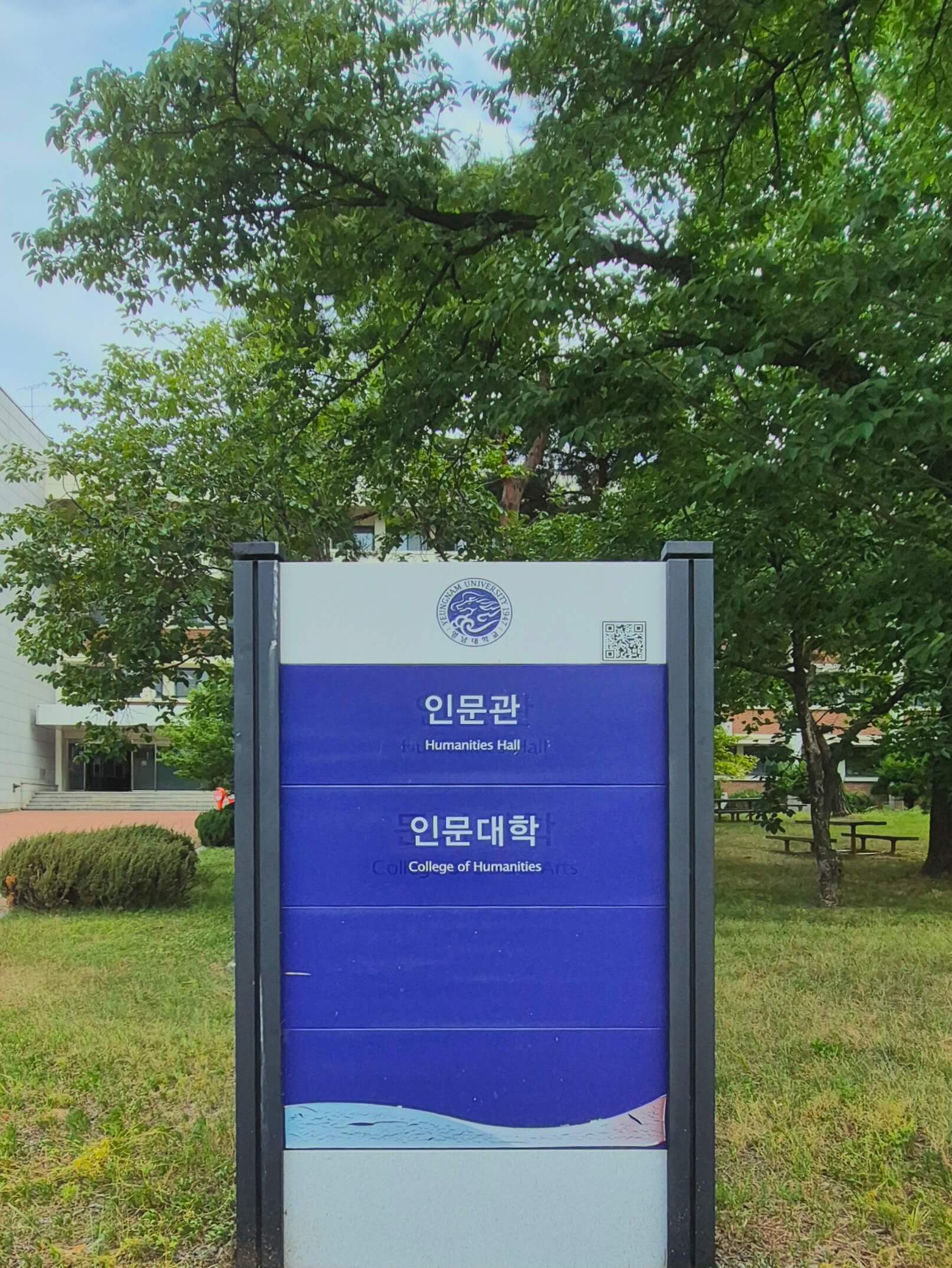 영남대학교의 건물 안내판. 파란색 배경 위로 흰 글씨로 '인문관','인문대학'이라고 적혀있고 각각 글씨 밑에 작게 영어 번역이 적혀있다