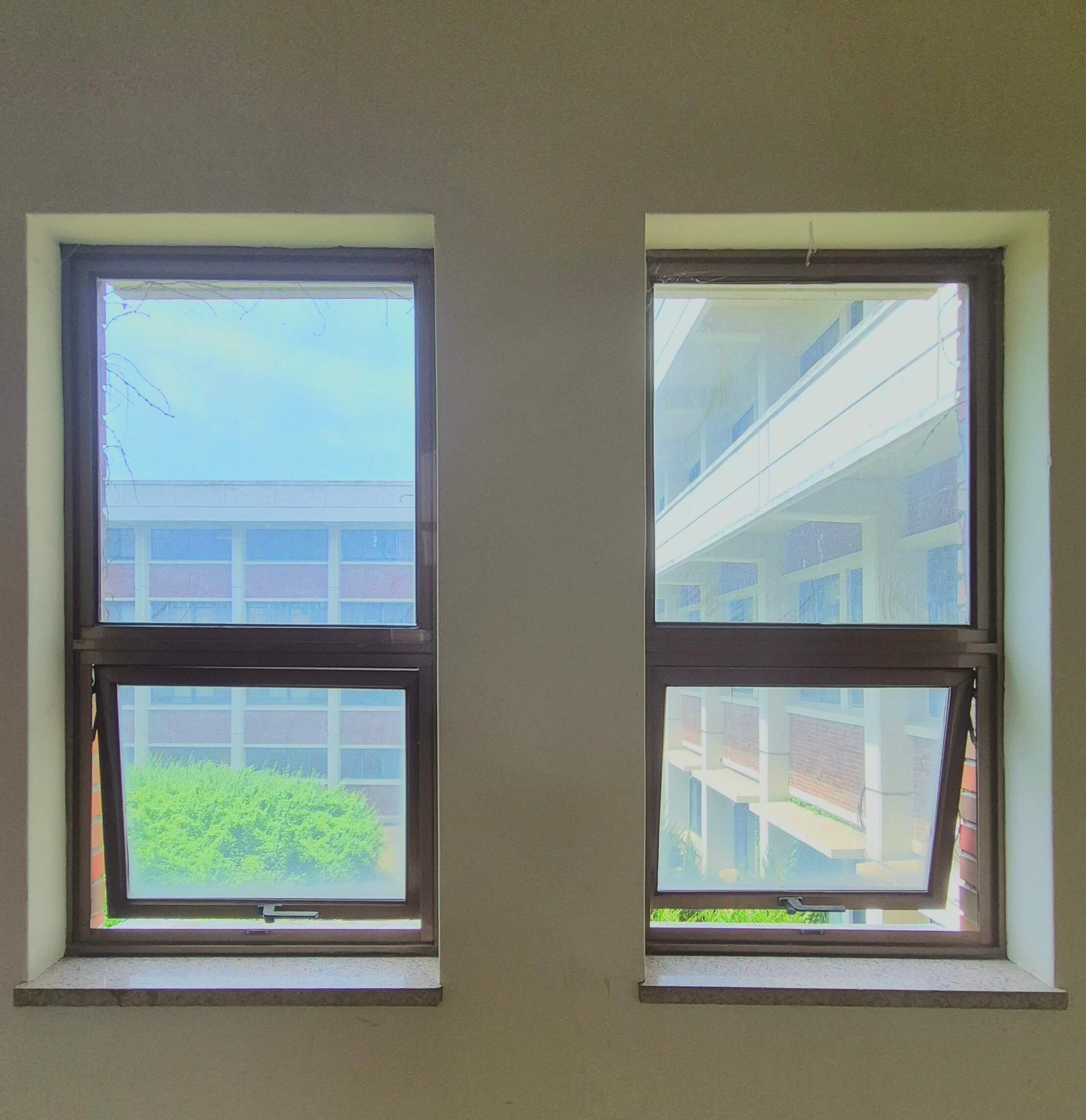 인문관 창문, 흰 벽 위로 검은 창틀로 된 직사각형 형태의 창문이 2개 있다. 정사가형이 위아래로 나란히 붙어 직사각형을 이루는 형티인데, 아래쪽 창문은 바깥으로 열려있다. 창문 너머로는 건물과 나무가 보인다.