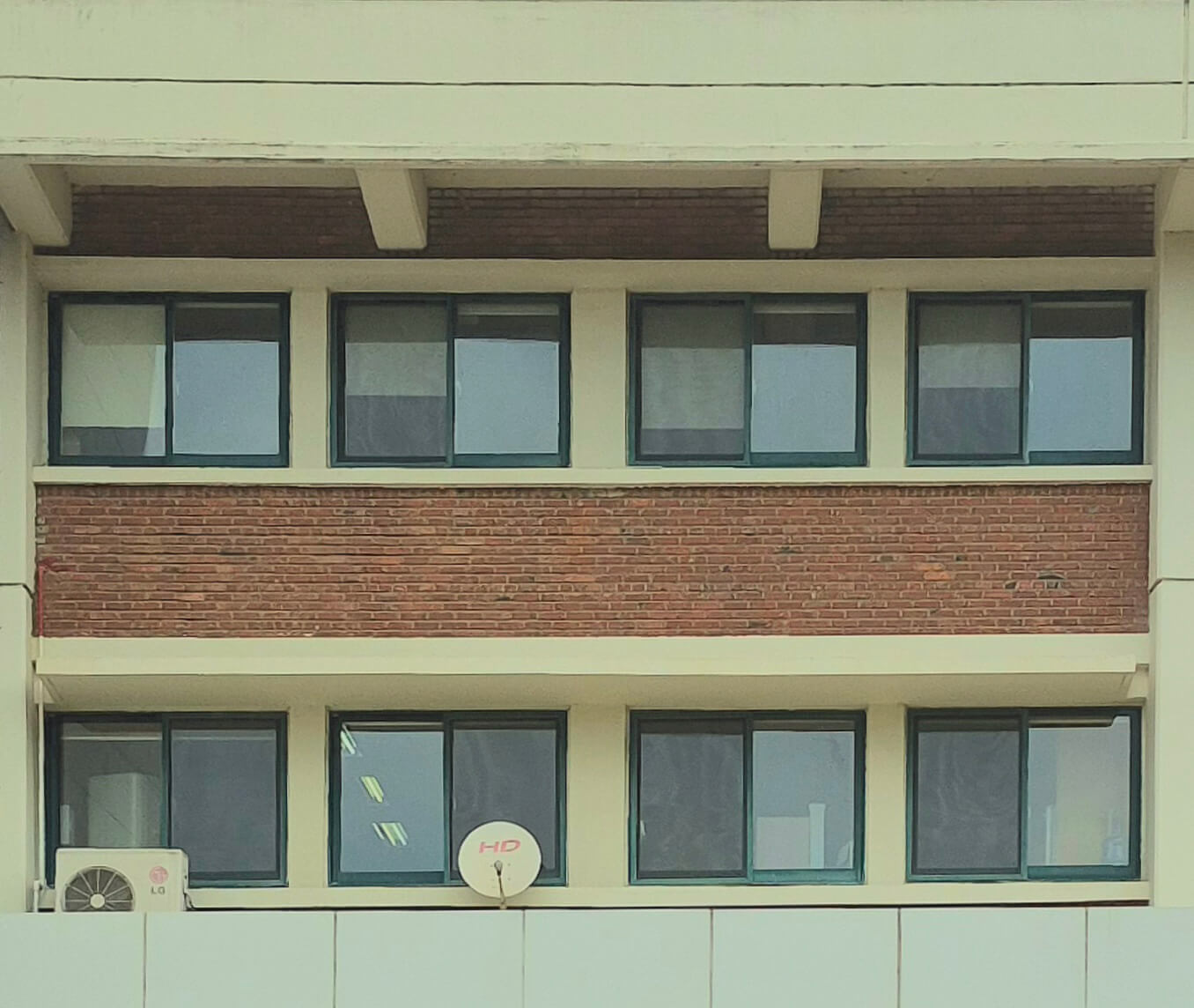 인문관 창문, 흰 벽 위로 녹색 창틀로 된 직사각형 형태의 창문이 한 줄에 4개씩 2줄이 있다. 줄 사이엔 붉은 벽돌벽이 있다. 아래쪽 줄의 가장 왼쪽 창문은 실외기에 약간 가려져있고, 그 옆의 창문은 안테나에 약간 가려져 있다.