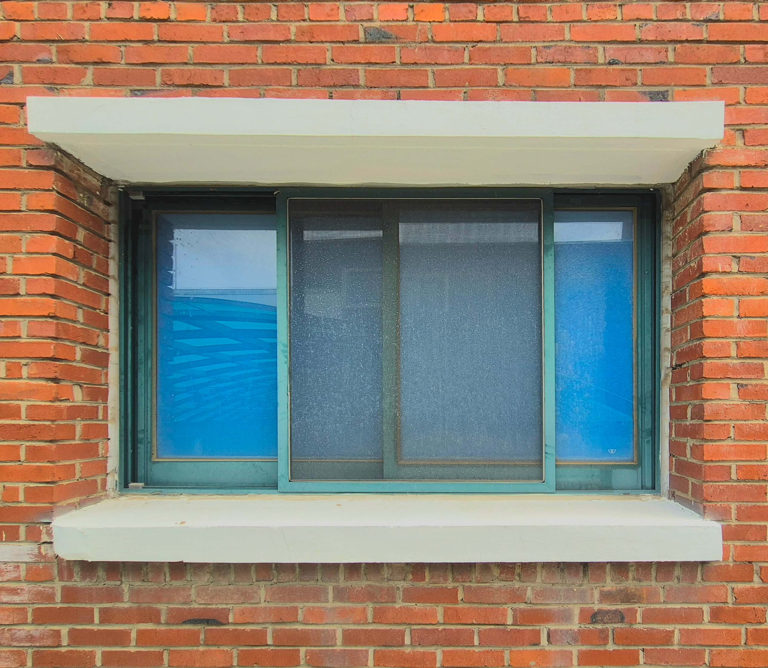 인문관 창문, 붉은 벽돌벽 위로 녹색 창틀로 된 직사각형 형태의 창문이다. 창문의 위 아래로 흰색 단이 있다. 정사각형 두 개가 가로롤 붙어 직사각형을 이루는 형태인데, 두 창문 사이에 반쯤 열린 창틀이 하나 있다.