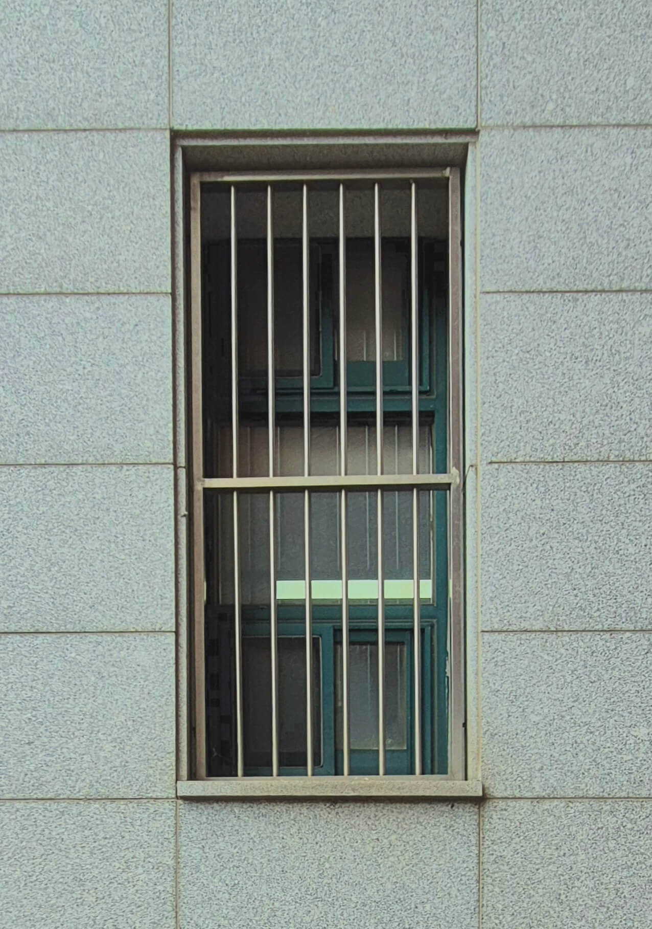 인문관 창문, 회색 벽 위로 세로로 긴 직사각형 형태의 창문이 있다. 창문에 가로로 6줄, 세로로 2줄로 나뉜 철창이 붙어있다. 그 안으로 녹색 창틀이 보인다.