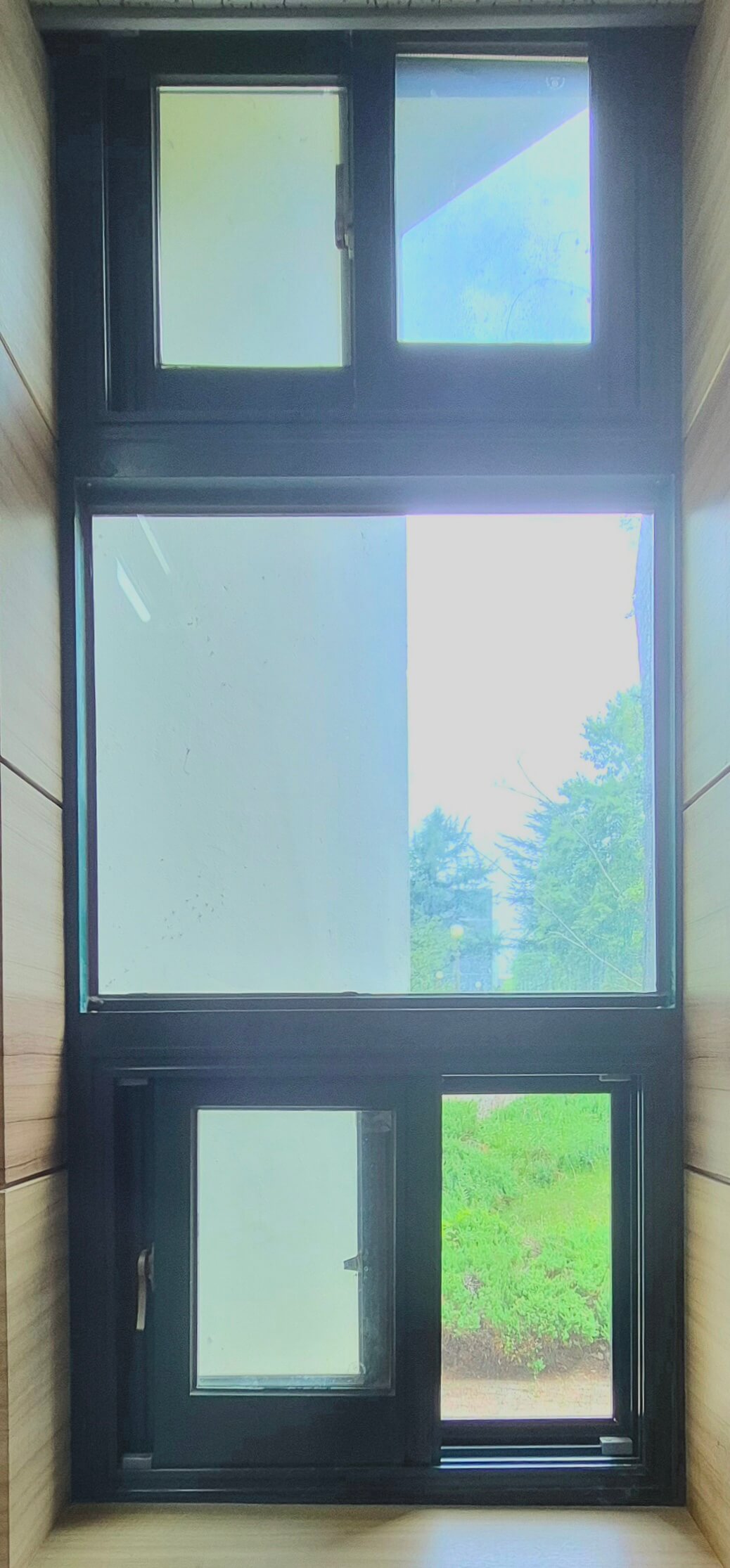 인문관 창문, 나무 재질의 벽 위로 녹색 창틀로 된 직사각형 형태의 창문이다. 창문 세 개가 위아래로 나란히 붙어 세로로 긴 직사각형 형태를 이룬다. 중가늬 창문은 위 아래에 있는 둘로 나뉜 창문과 달리 통창이다. 창문 너머로 햇빛이 비치고 회색 벽과 나무가 보인다.