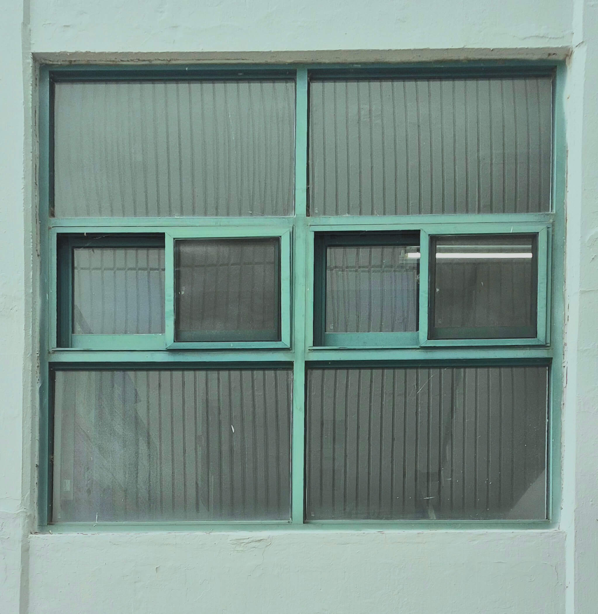 자연과학대학 창문, 희 벽 위로 연녹색 창틀로 된 정사각형 형태의 창문이 있다. 위 아래는 가로로 긴 직사각형 두 개가 옆으로 나란히 붙어있고, 가운데는 정사각형 네 개가 옆으로 나란히 붙어 큰 정사각형 형태를 이루고 있다. 창문의 유리창에 반대편의 벽이 비친다.