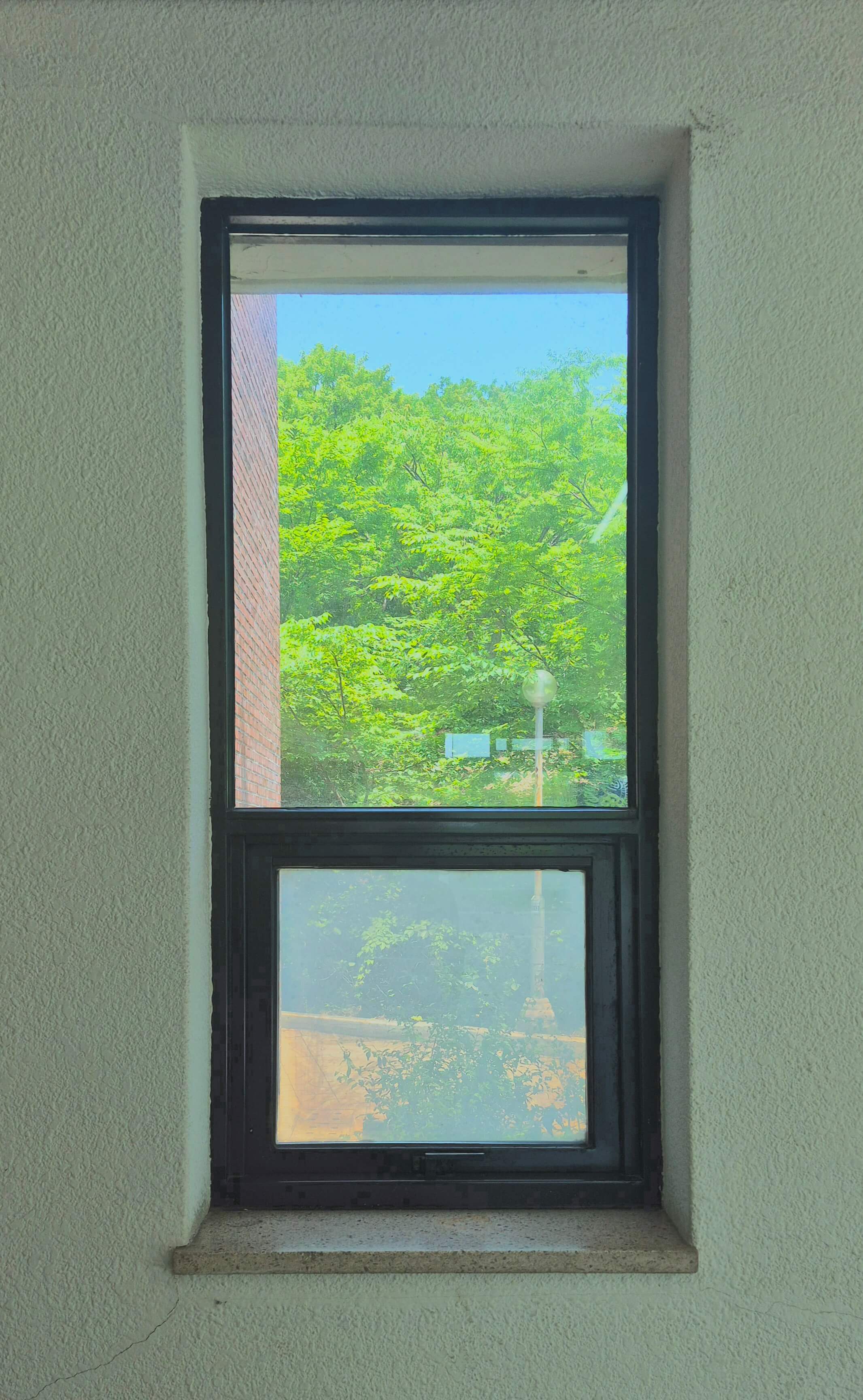 디자인관 창문, 흰 벽 위로 검은 창틀로 된 직사각형 형태의 창문이 있다. 위쪽에 세로로 긴 직사가형이 있고, 그 아래로 정사각형이 붙어있다. 위쪽 창문은 아래쪽에 비해 창틀이 얇다. 창문 너머로 가로등과 나무가 보인다.