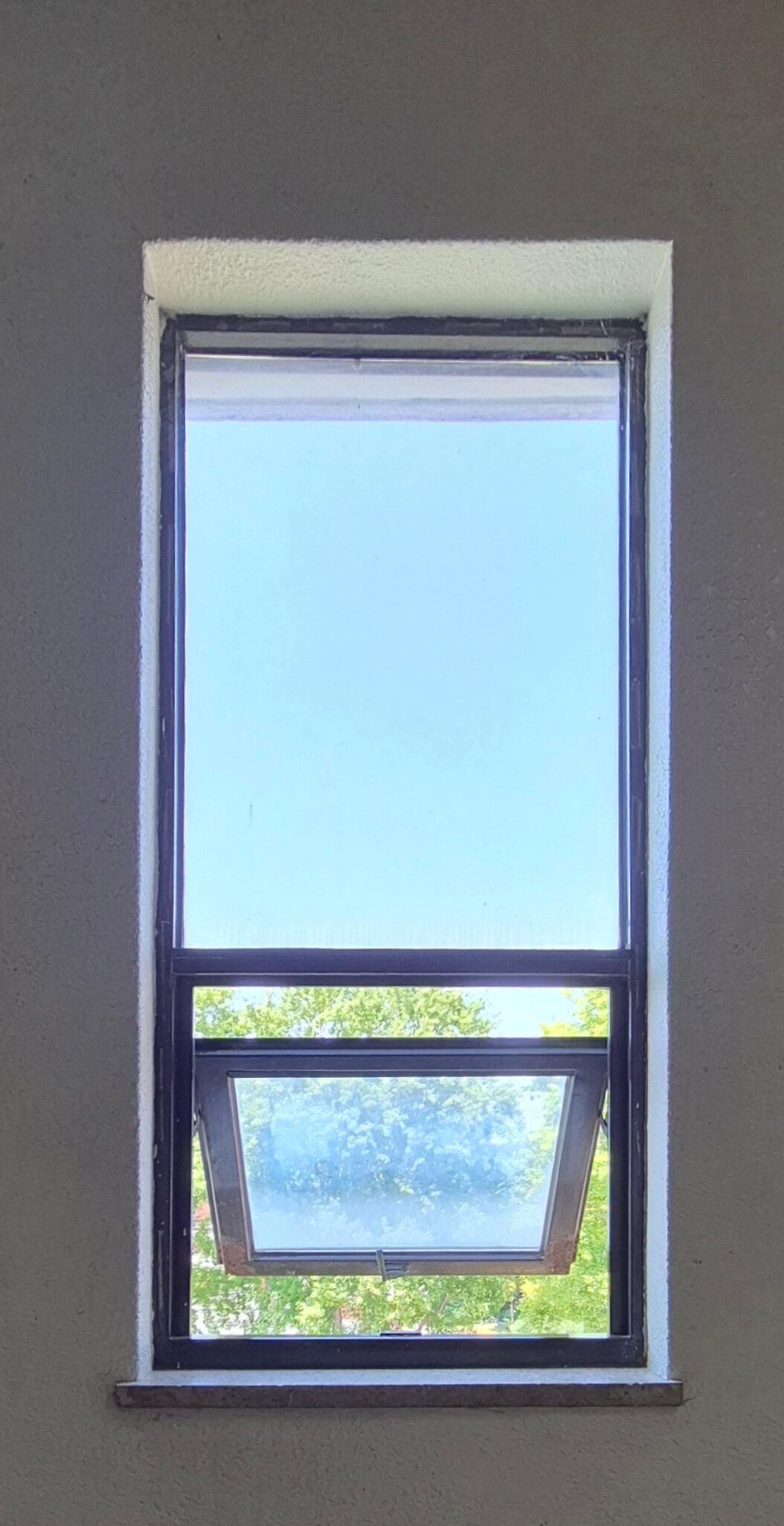 디자인관 창문, 흰 벽 위로 검은 창틀로 된 직사각형 형태의 창문이 있다. 위쪽에 세로로 긴 직사가형이 있고, 그 아래로 정사각형이 붙어있다. 위쪽 창문은 아래쪽에 비해 창틀이 얇다. 아래쪽 창문은 바깥으로 반쯤 열려있다. 창문 너머로 나무의 윗부분이 보인다.