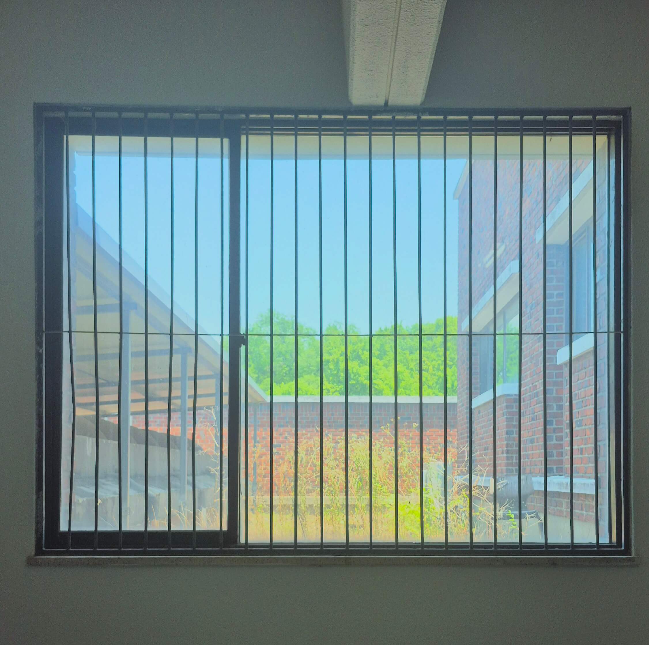 디자인관 창문, 흰 벽 위로 검은 창틀로 된 직사각형 형태의 2분할돤 창문이 있다. 왼쪽의 너비가 오른쪽에 비해 좁은 형태이다. 유리창 위로 얇은 철창이 달려있다. 창문 너머로 붉은 벽돌벽 건물의 일부와 풀, 그 너머로 벽돌 담장과 그 뒤의 나무가 보인다.