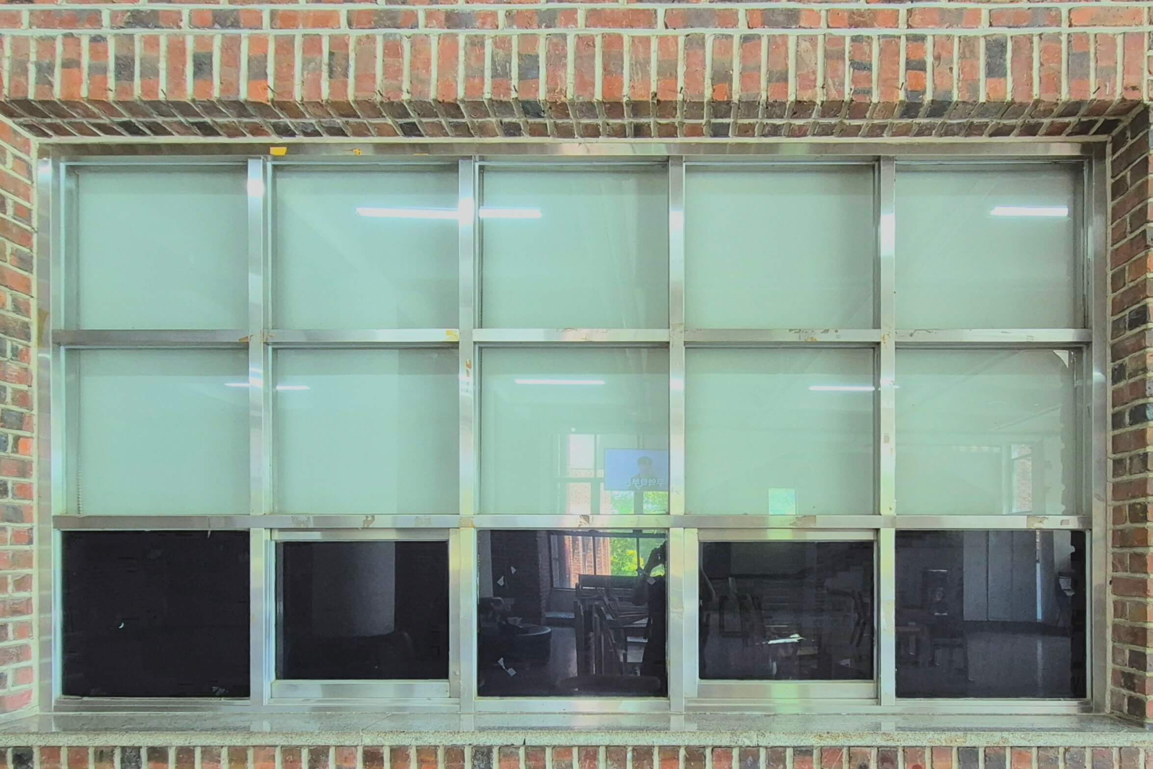 디자인관 창문, 붉은 벽돌벽 위에 흰 창틀로 된 직사각형 형태의 창문이 있다. 정사각형이 가로로 5개싹, 세로로 3개씩 총 15개가 합쳐져 직사각형을 이루는 형태이다. 위쪽 두 칸은 반대편에서 블라인드가 쳐져있어 흰색으로 보이고, 맨 아래쪽 한 칸은 반대편이 비쳐 보인다.