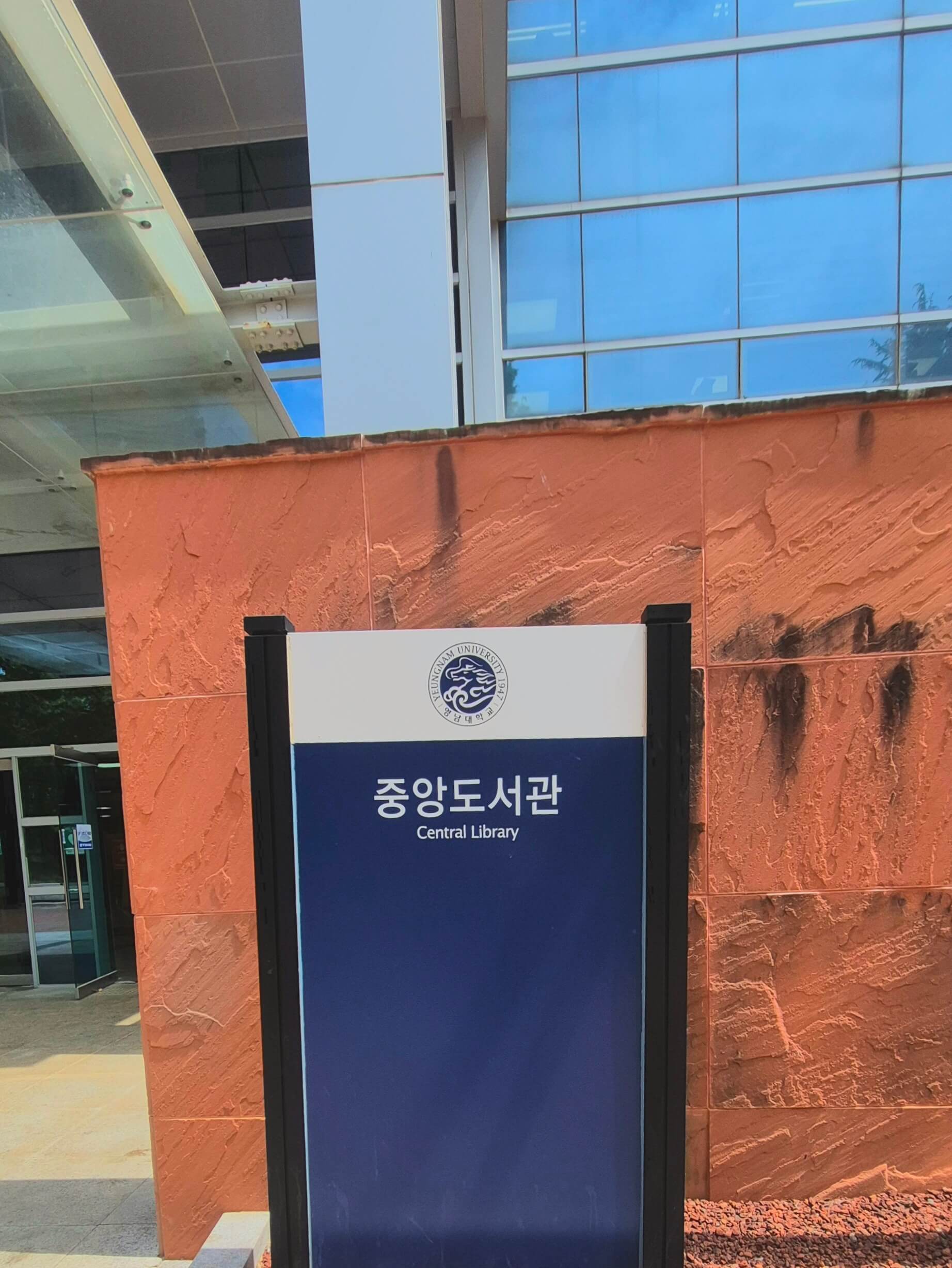 영남대학교의 건물 안내판. 파란색 배경 위로 흰 글씨로 '중앙도서관'이라고 적혀있고 글씨 밑에 작게 영어 번역이 적혀있다