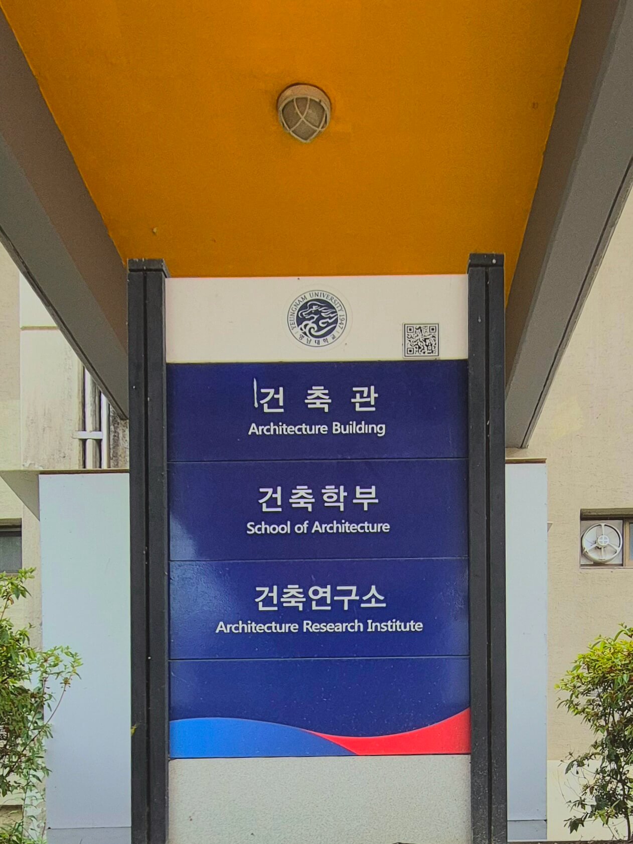 영남대학교의 건물 안내판. 파란색 배경 위로 흰 글씨로 '건축관','건축학부','건축연구소'라고 적혀있고 각각 글씨 밑에 작게 영어 번역이 적혀있다
