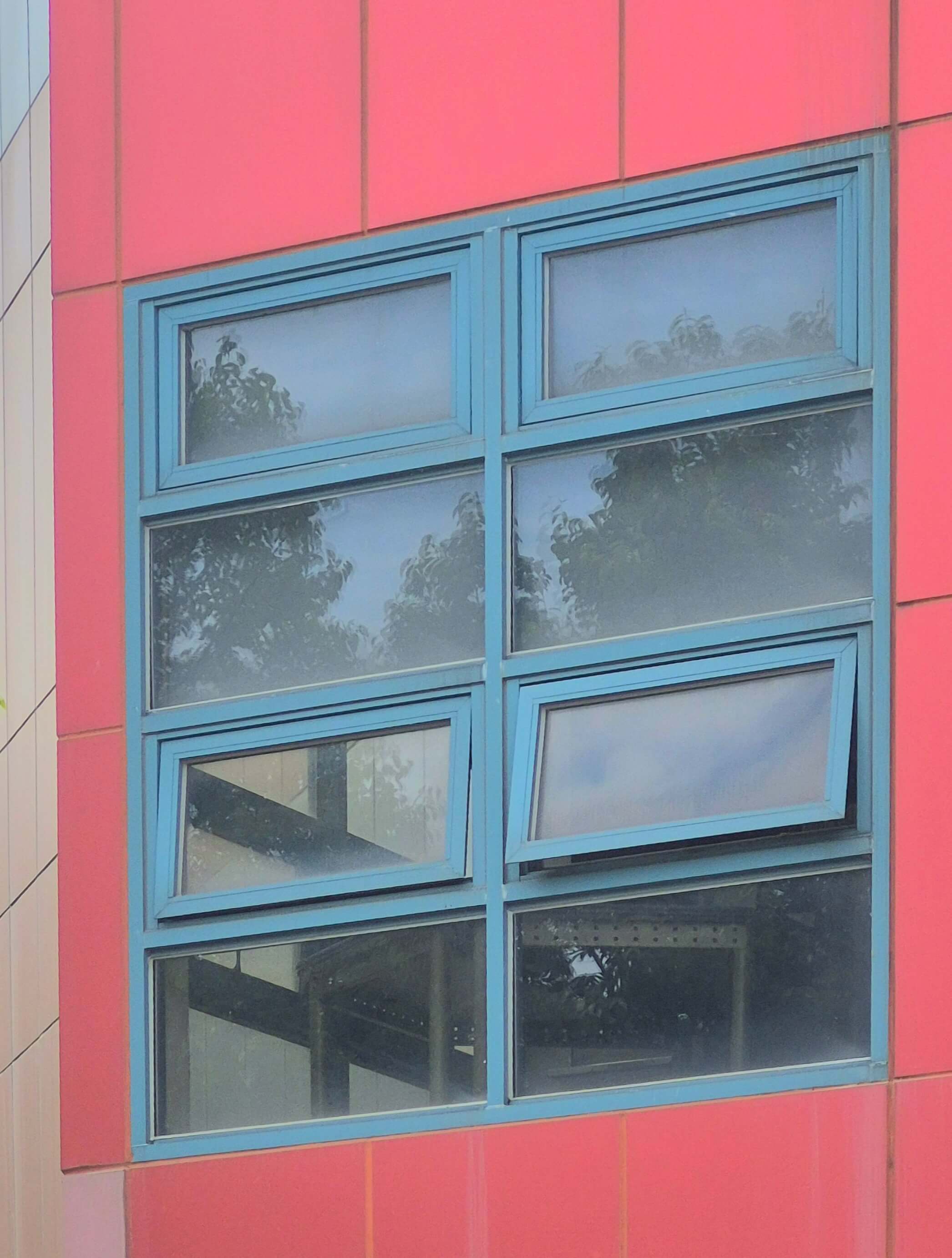 건축관 창문, 빨간 벽 위에 청록색 창틀로 된 직사각형 형태의 창문이 있다. 가로로 2개씩, 세로로 4개씩 붙어있다. 위에서 3번째 줄의 두 창문은 밖으로 열려있다.